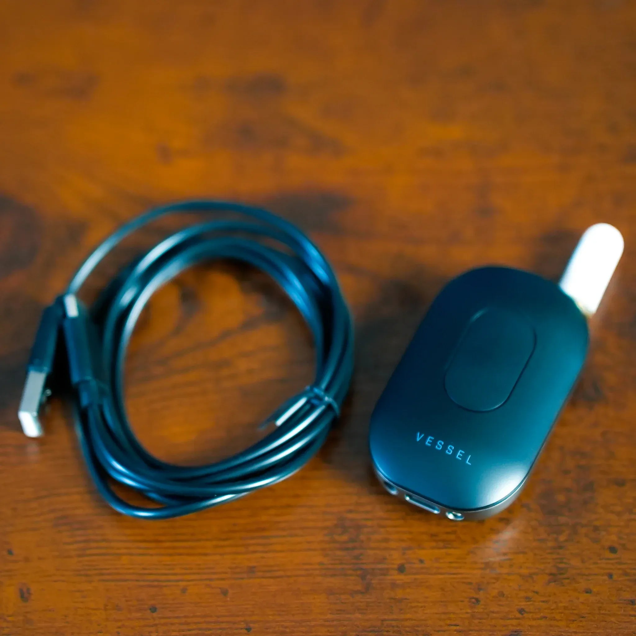 Top-down close-up of the Freeze Pipe Vape Pen on a warm wooden surface, showing its coiled cable and matte body.