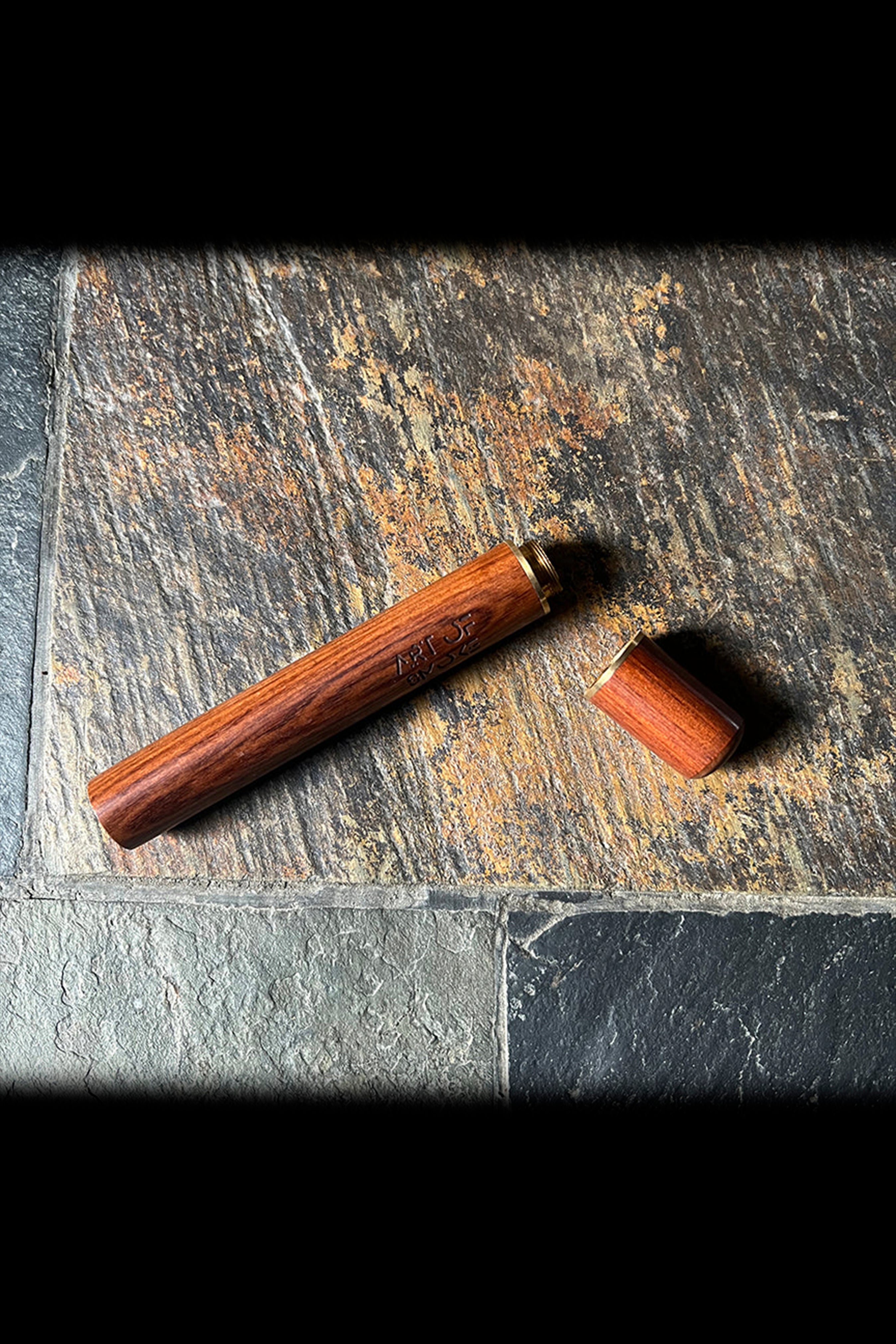 Wooden one-hitter pipe and cap on a textured stone surface.
