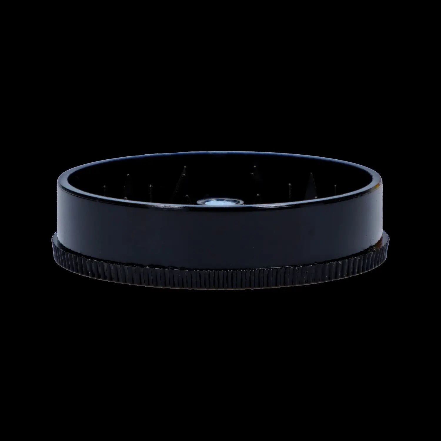 Low-angle close-up of the Black Skull Mini Travel Grinder showing its glossy black rim, interior teeth, and textured base against a black background
