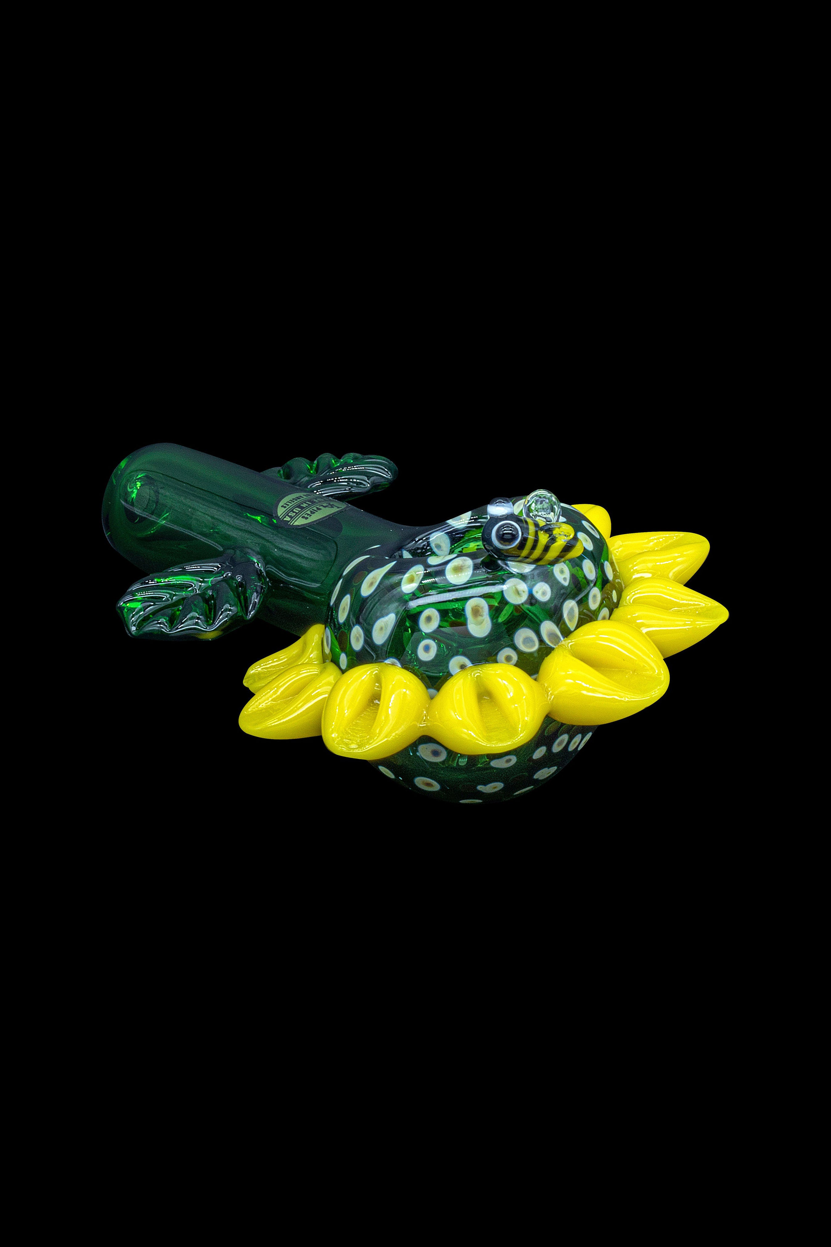 Hand-blown glass cannabis rig shaped like a frog with yellow floral accents, isolated on a black background.
