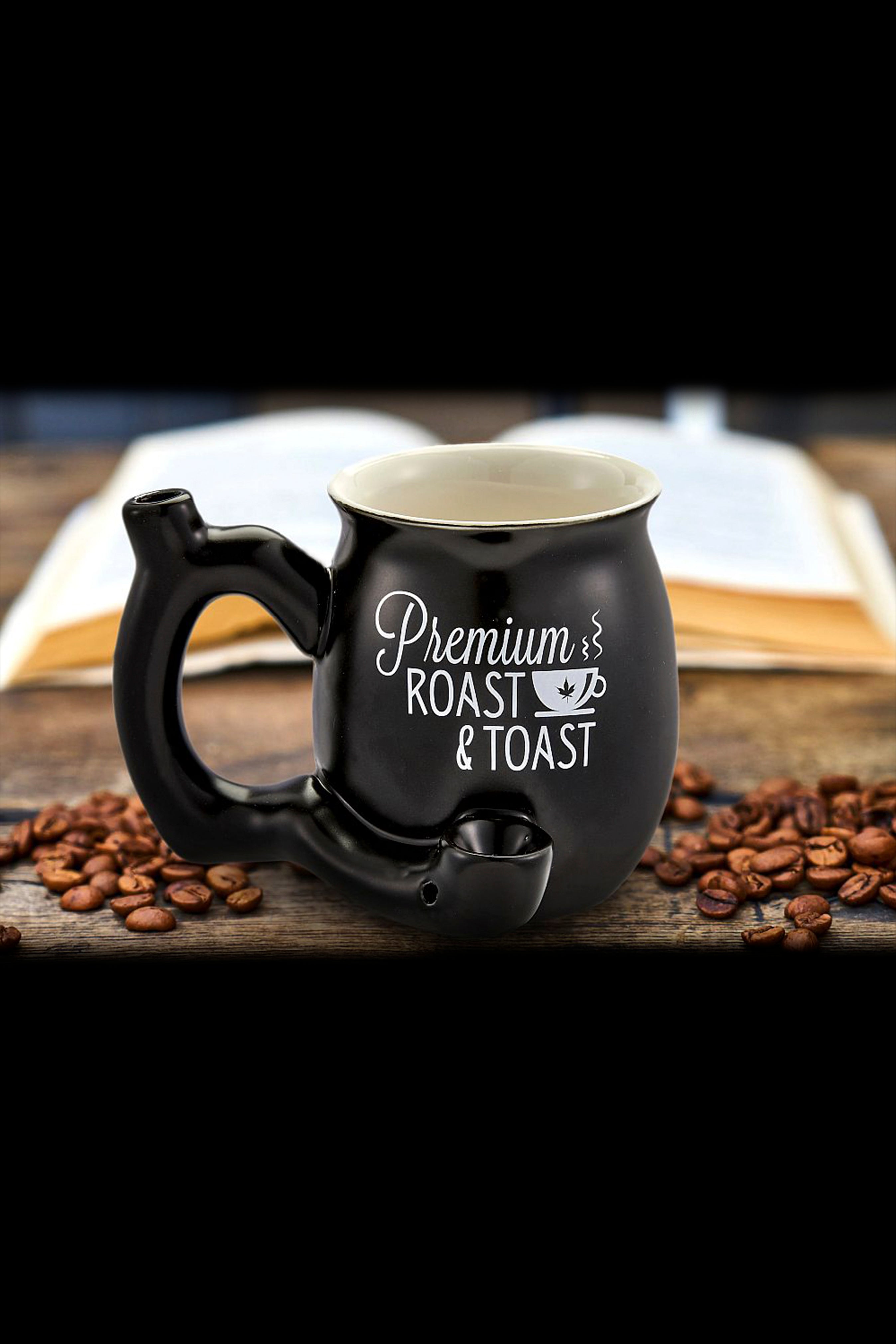 Black ceramic mug with a built-in pipe, labeled “Premium Roast & Toast,” resting on coffee beans.