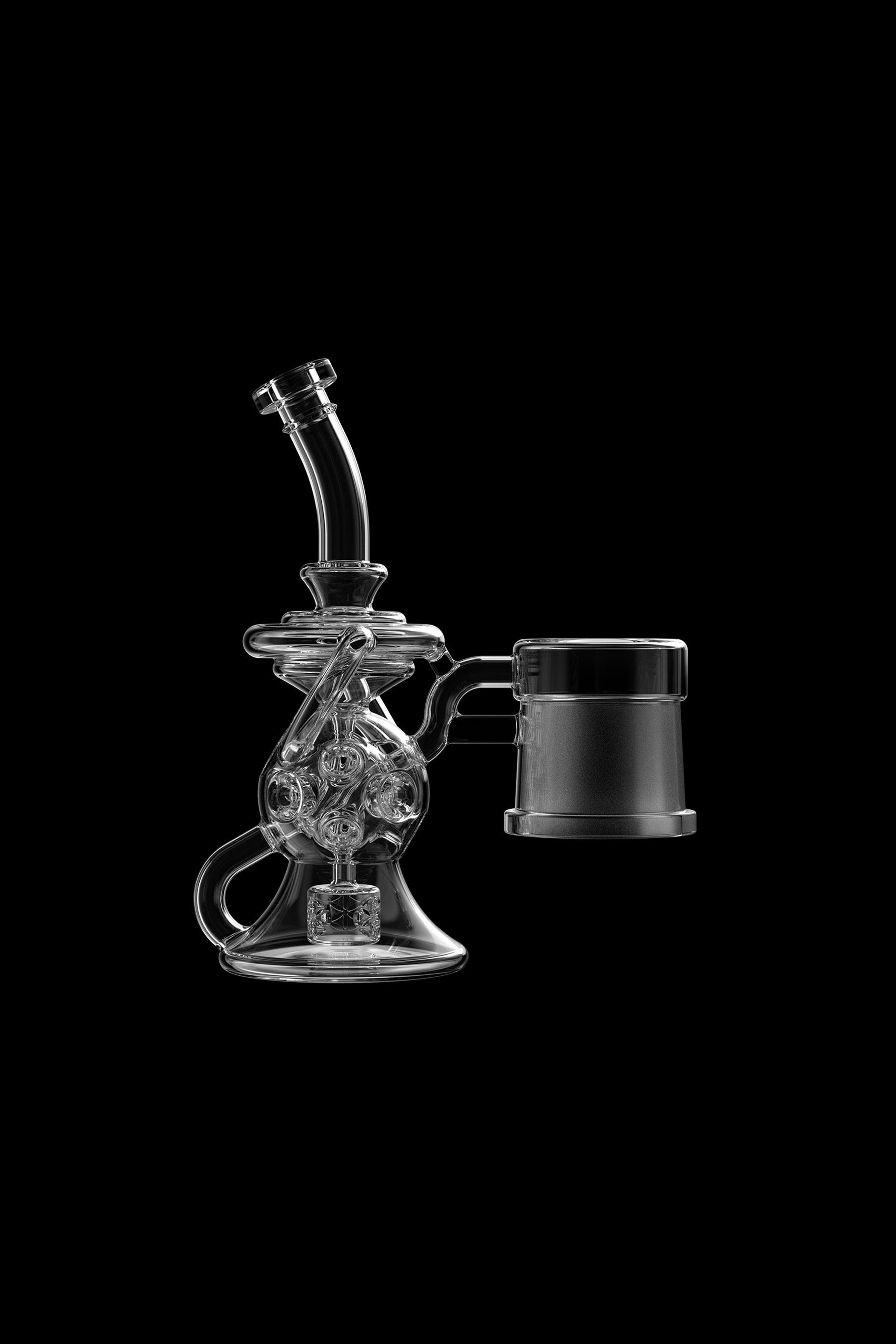 Clear glass rig with intricate bubbler design and accompanying glass cup, isolated on black.