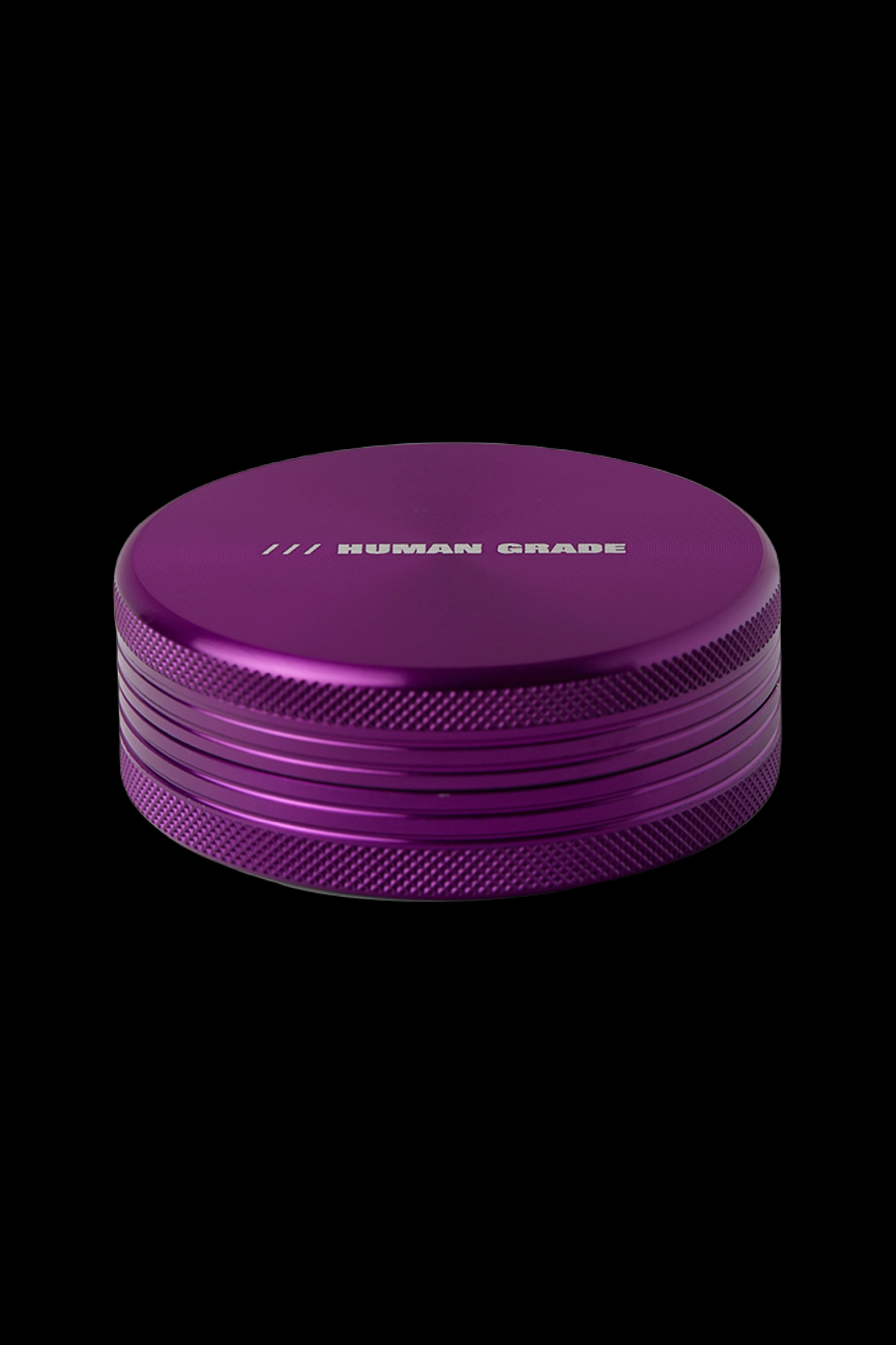 Purple cannabis grinder with “HUMAN GRADE” etched on top, isolated on a black background.