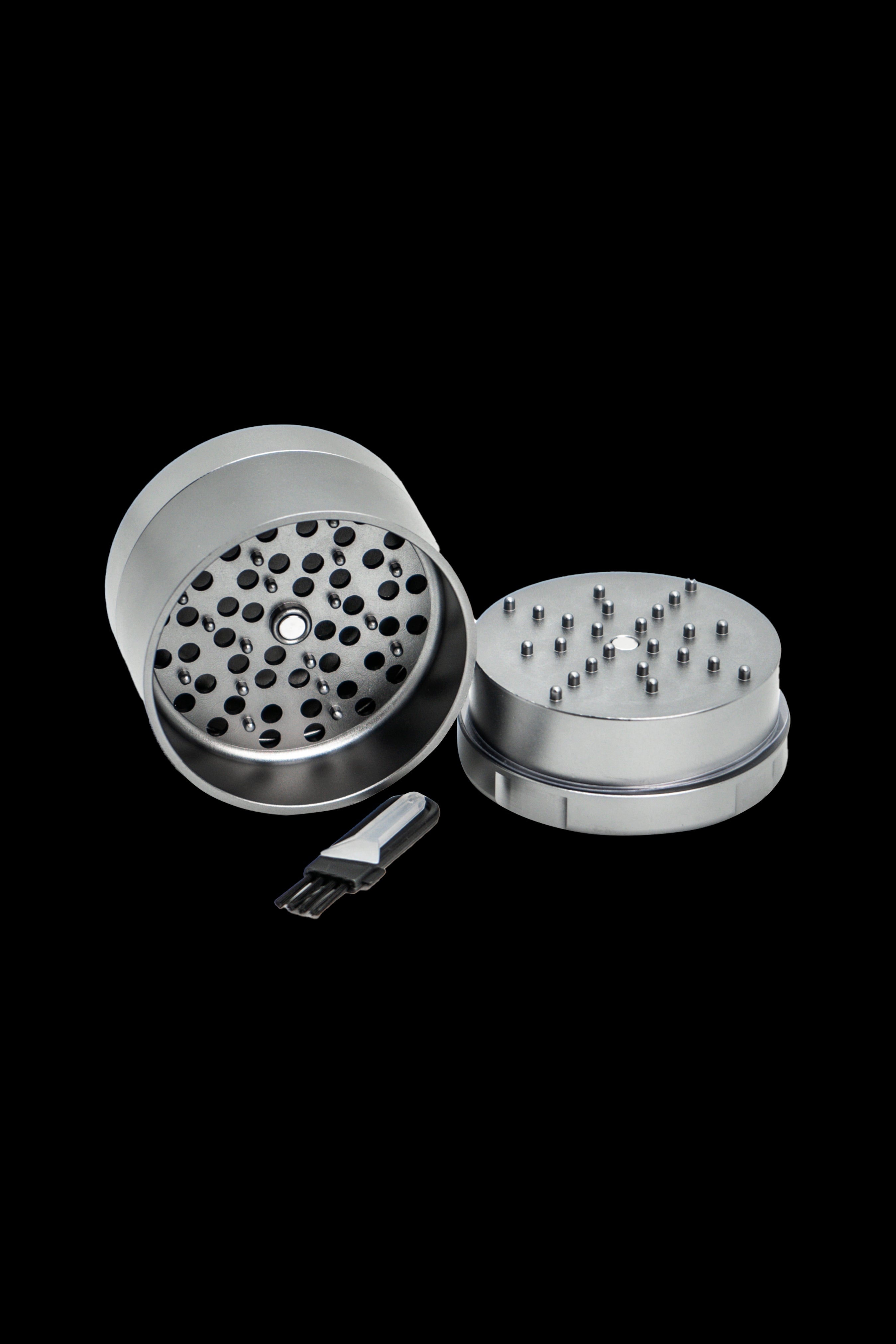 Silver cannabis grinder disassembled with included scraper tool, isolated on a black background.