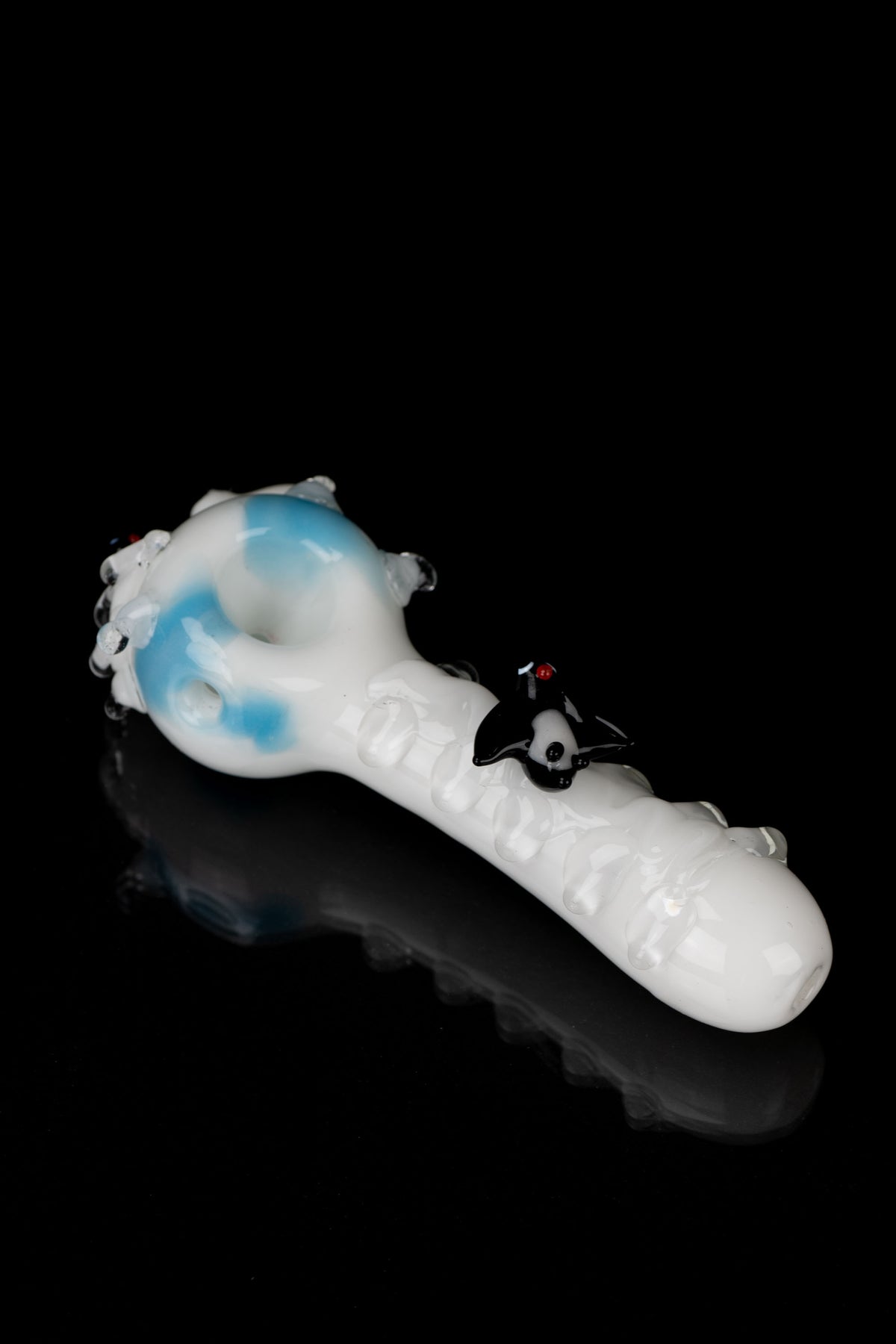 Glass pipe with blue and white swirling patterns, featuring a sculpted black skull detail, on a reflective black surface.