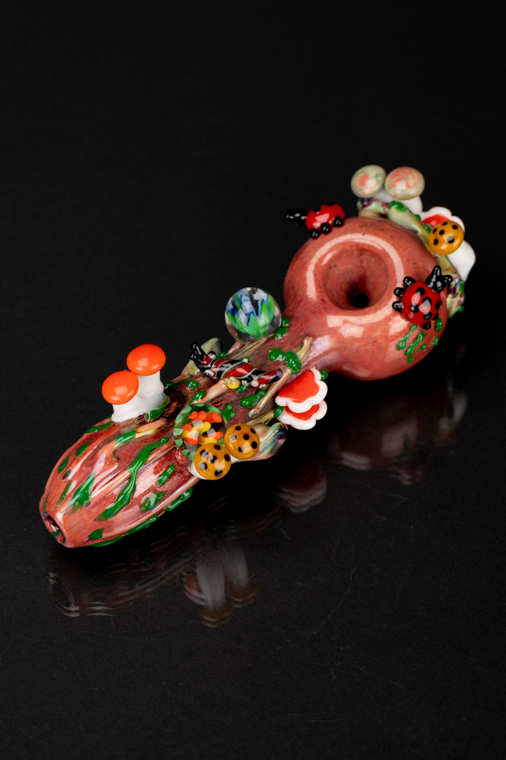 Hand-blown glass pipe adorned with colorful mushroom designs, studio shot on a black reflective surface.