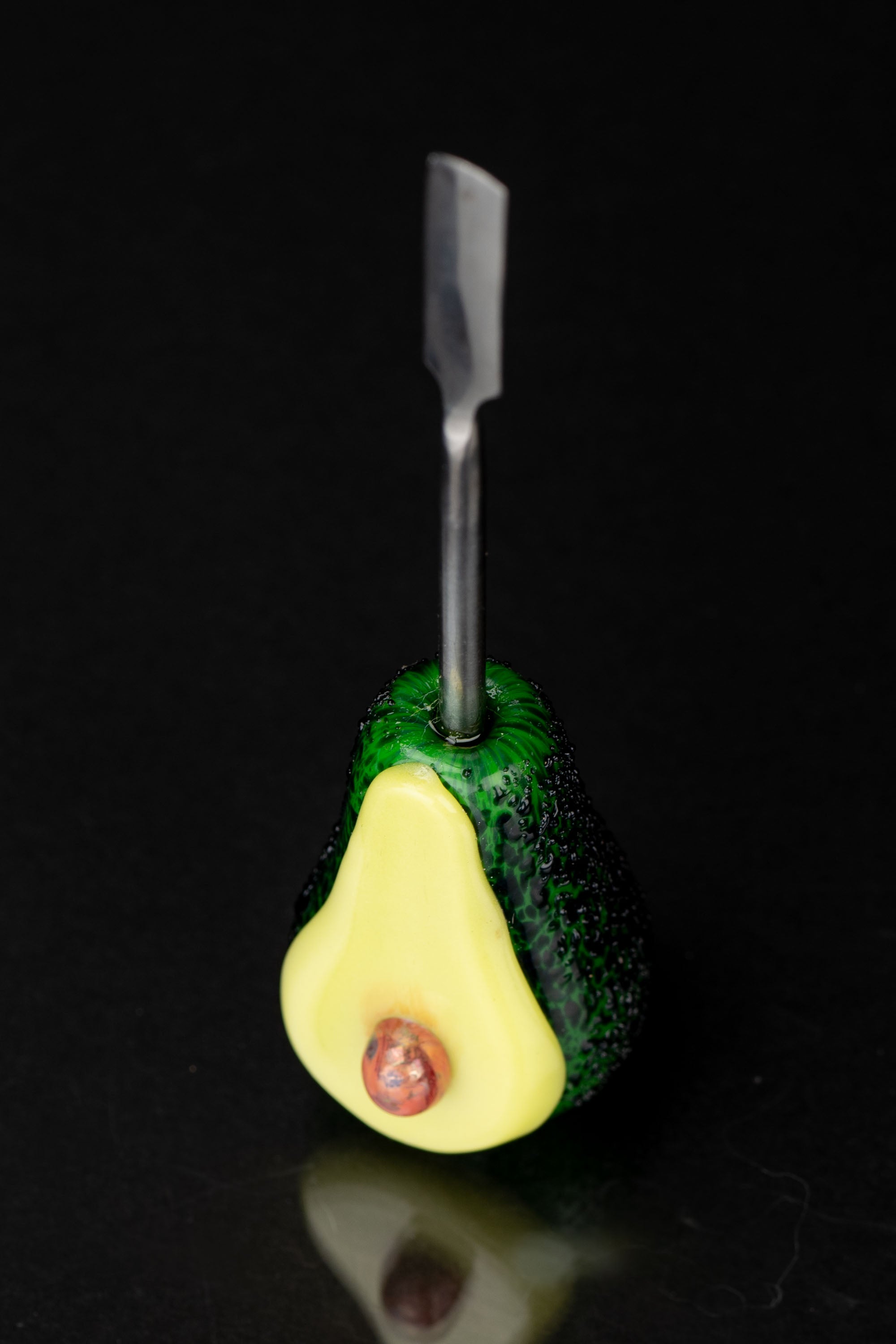 A glass avocado-shaped dab rig with a titanium carb cap inserted, set against a black background.