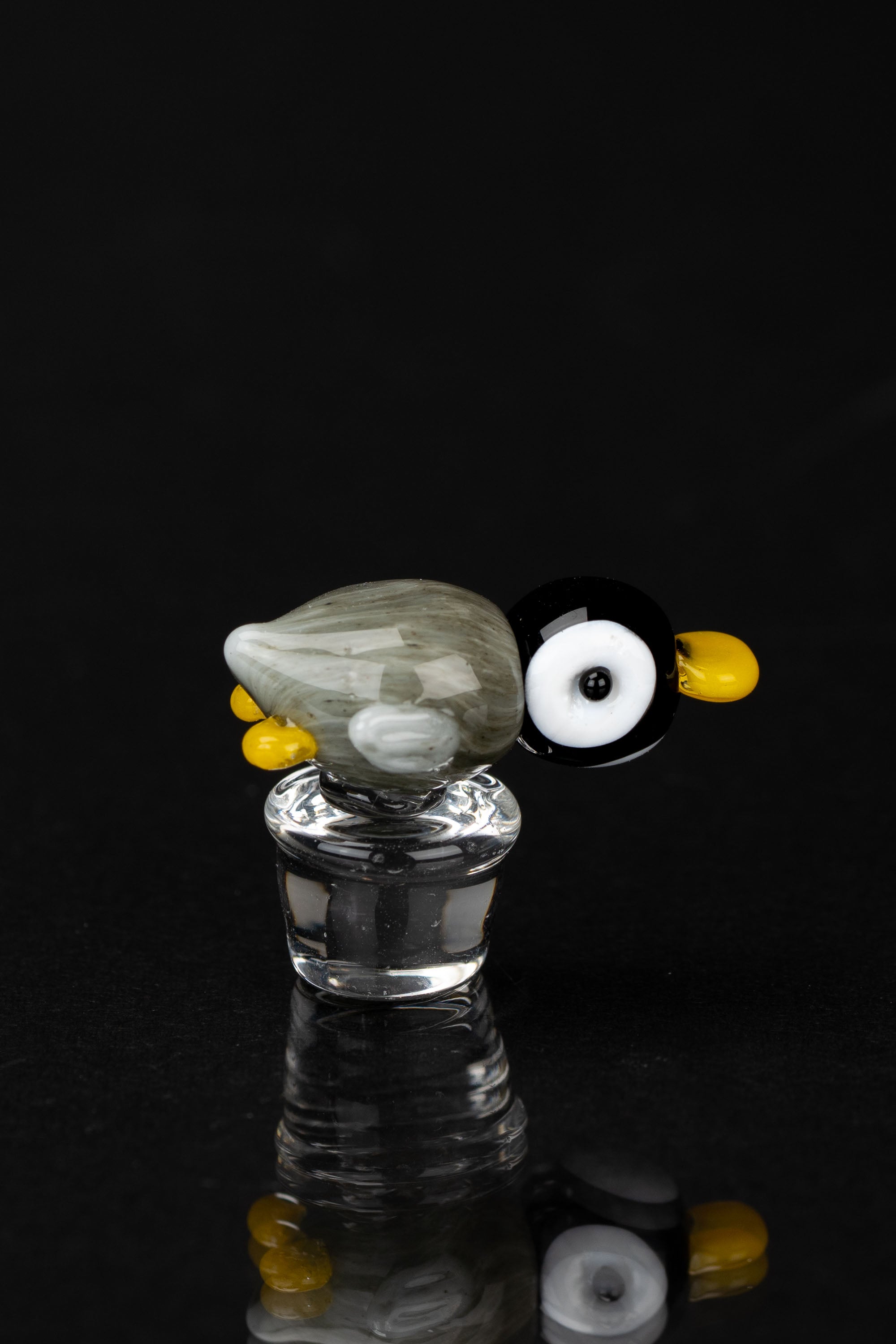 Glass cannabis accessory with a sculpted owl design, reflecting on a dark surface.