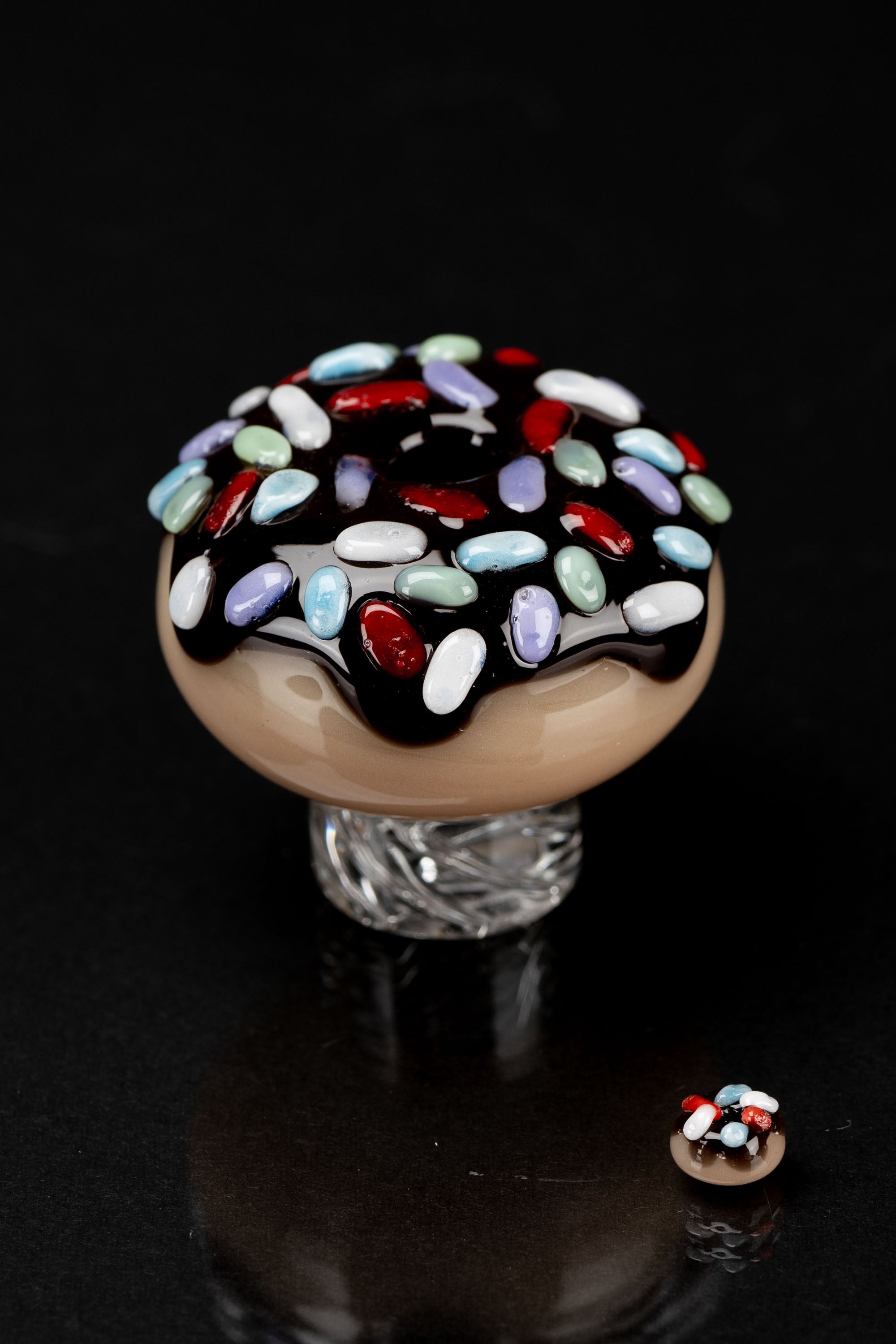 A colorful, hand-blown glass cap resembling a sprinkle-covered donut, likely used as a cannabis accessory.