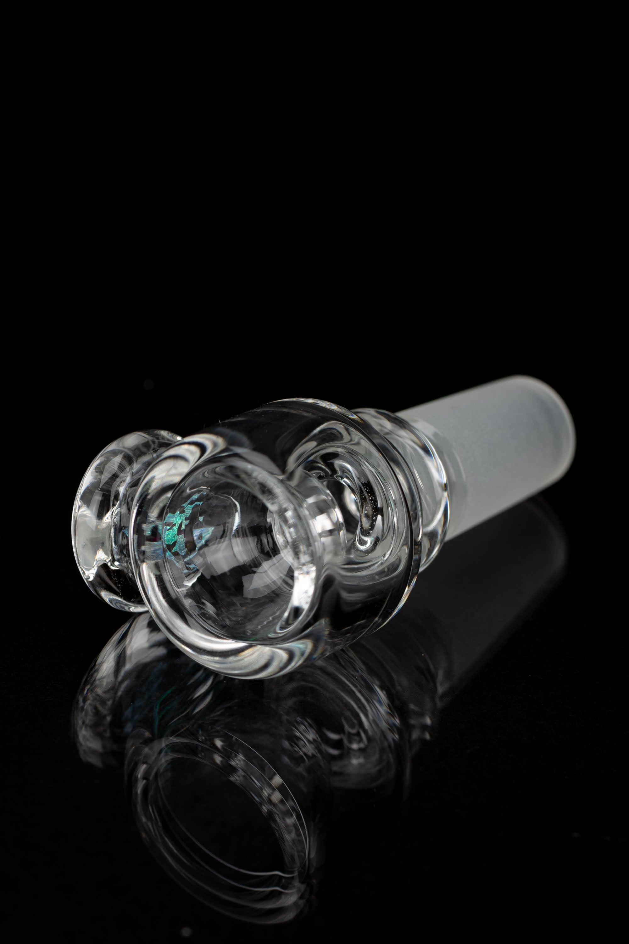 Clear glass cannabis bowl with intricate swirling design, reflecting on a dark surface.