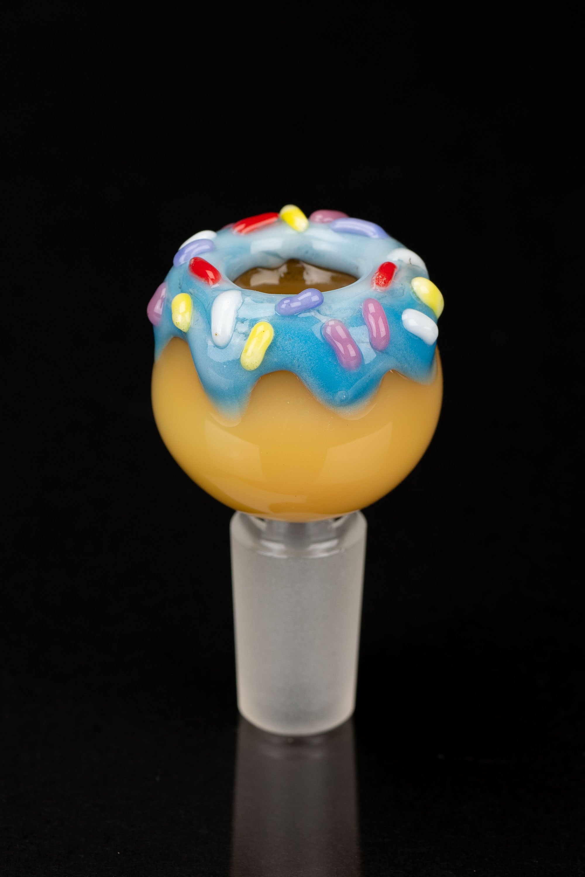 Glass cannabis water pipe shaped like a frosted donut with sprinkles, isolated on black.
