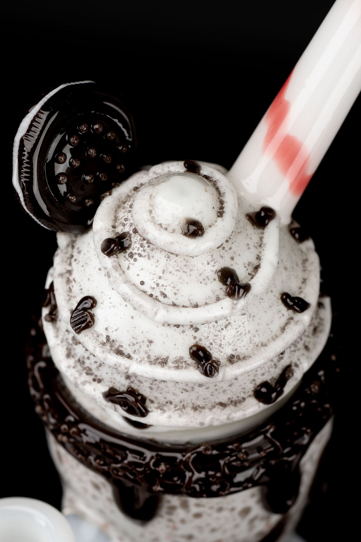 A close-up, top-down view of a chocolate milkshake in a glass, drizzled with chocolate sauce and topped with chocolate chips, alongside a small, dark cannabis accessory.