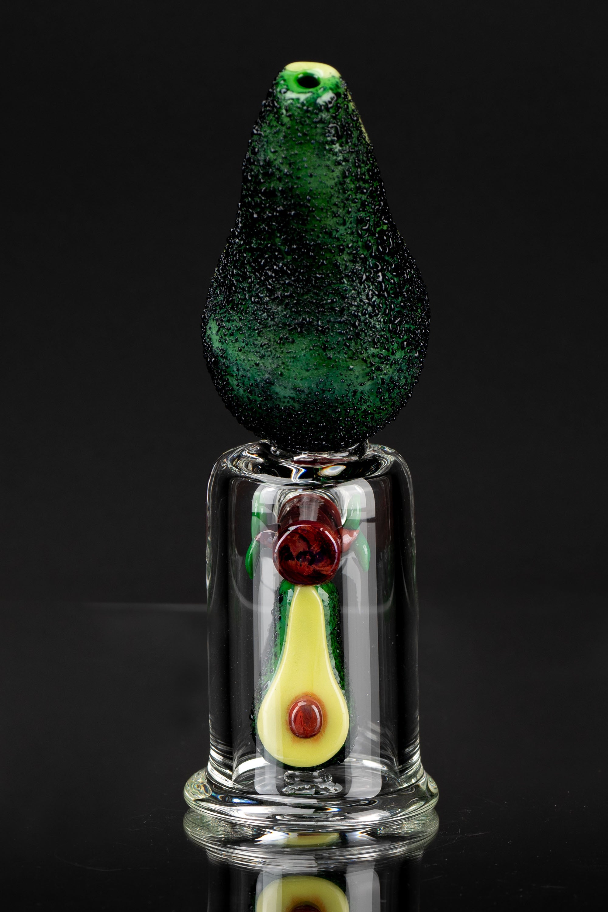 Hand-blown glass dab rig shaped like an avocado with colorful internal accents, reflecting on a glossy surface.