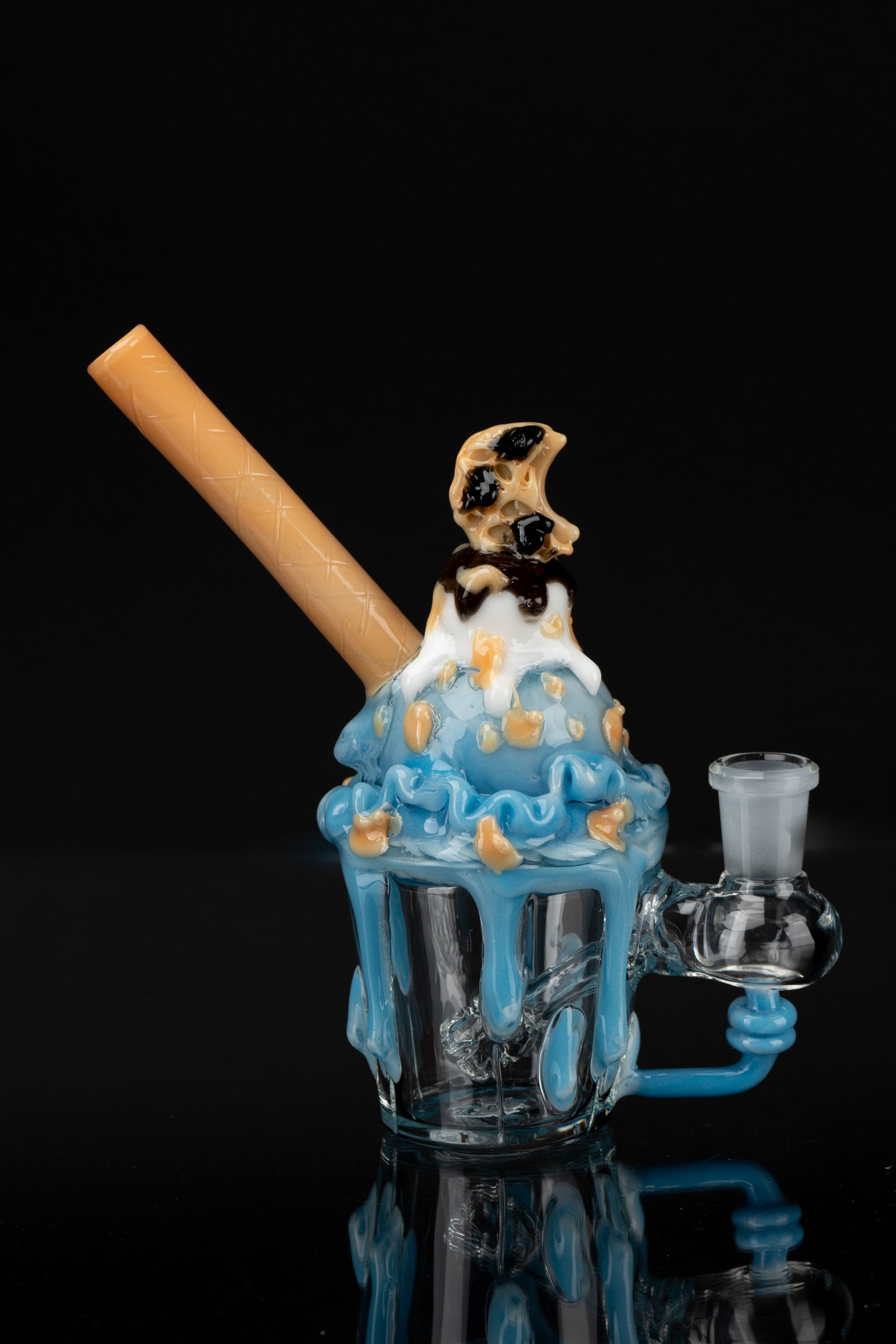 Blue glass water pipe shaped like an ice cream cone with chocolate drizzle and a wafer cookie on top, against a black background.