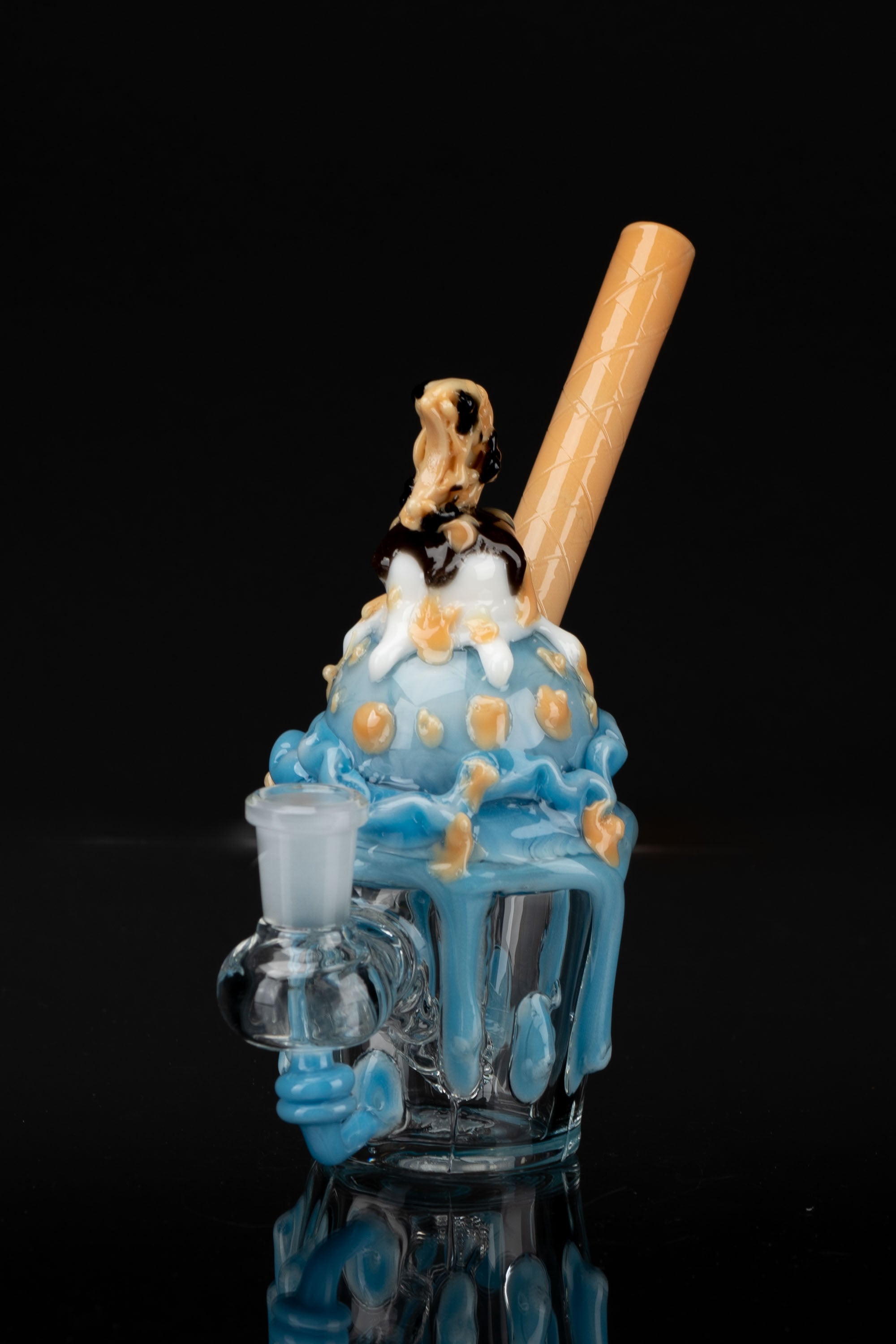 Hand-blown glass cannabis water pipe sculpted as a vibrant blue ice cream cone with caramel and gold accents, against a black background.