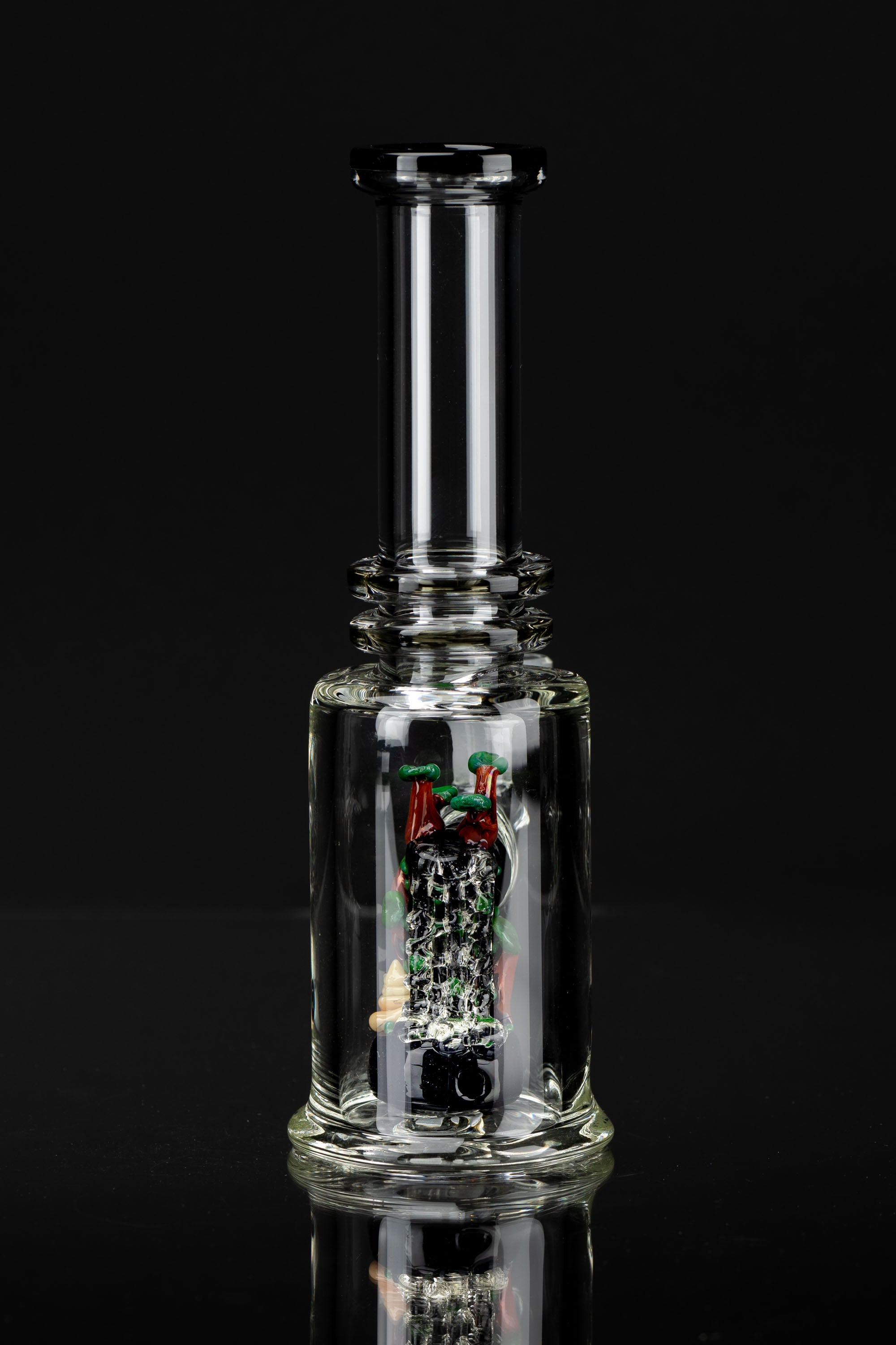 A clear glass bubbler with colorful glass artwork inside, reflecting on a dark surface.