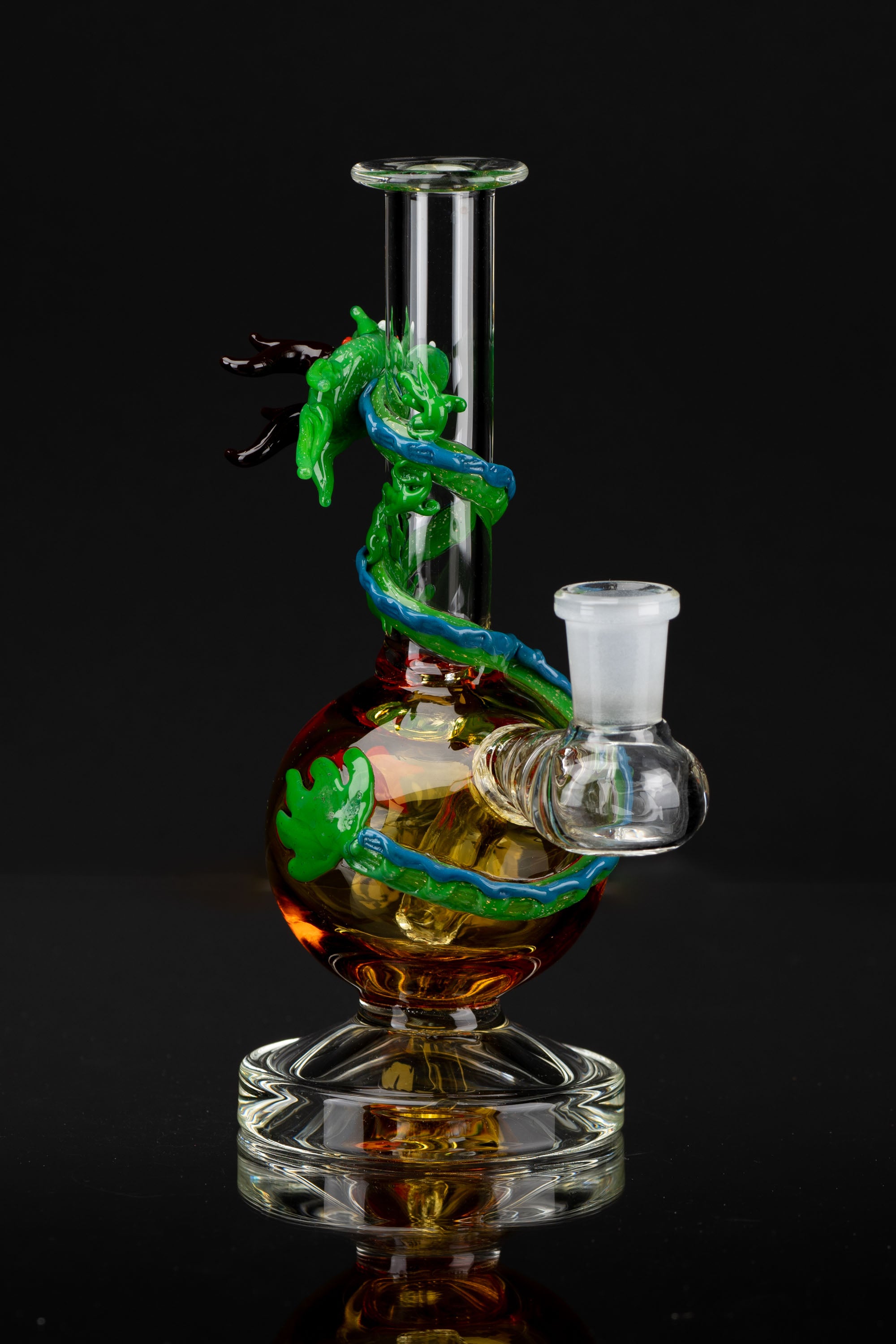 Hand-blown glass water pipe featuring a sculpted dragon, with amber and green coloring, against a black background.