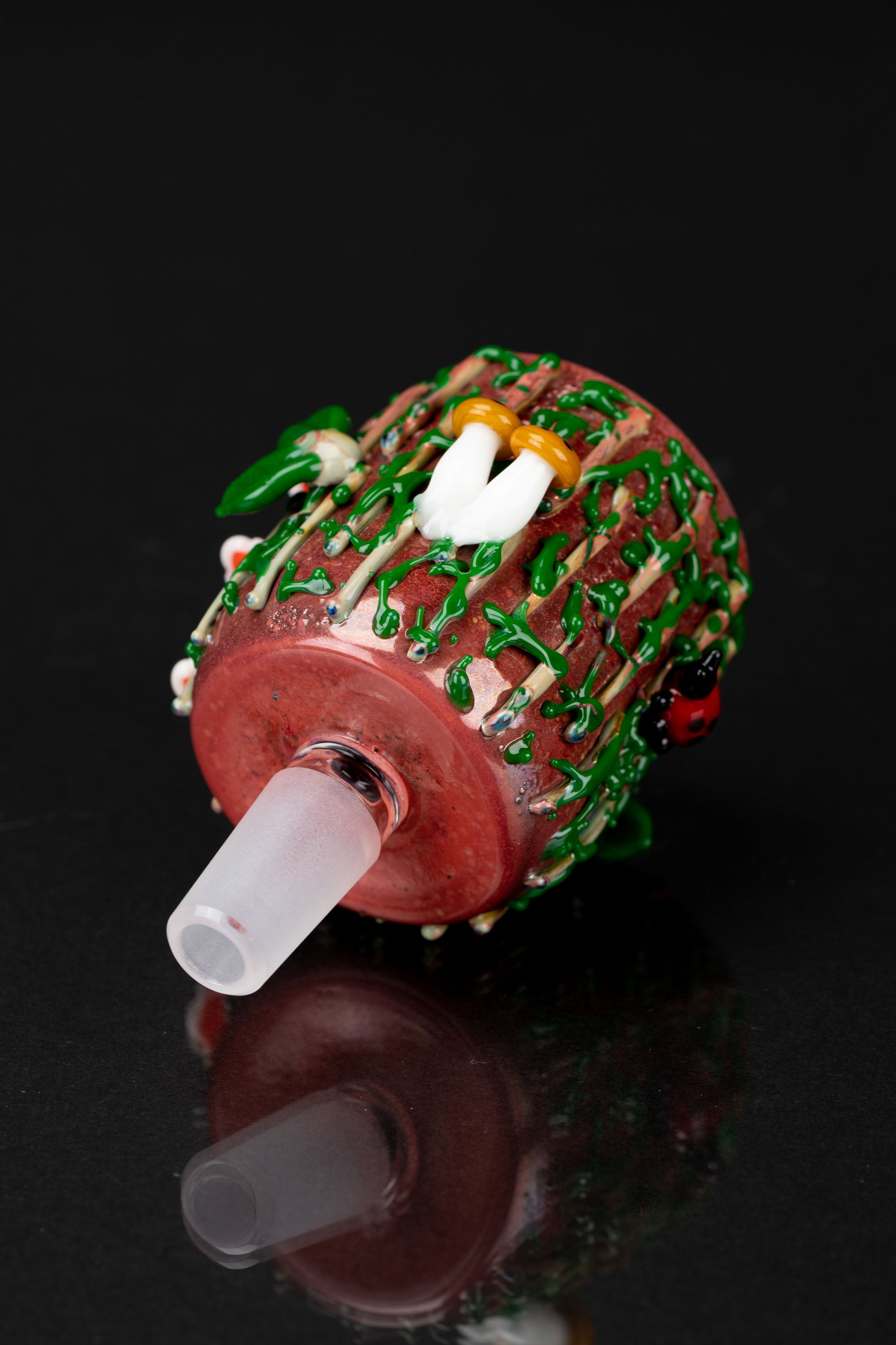 Hand-blown glass water pipe decorated with colorful mushroom designs, reflecting on a dark surface.