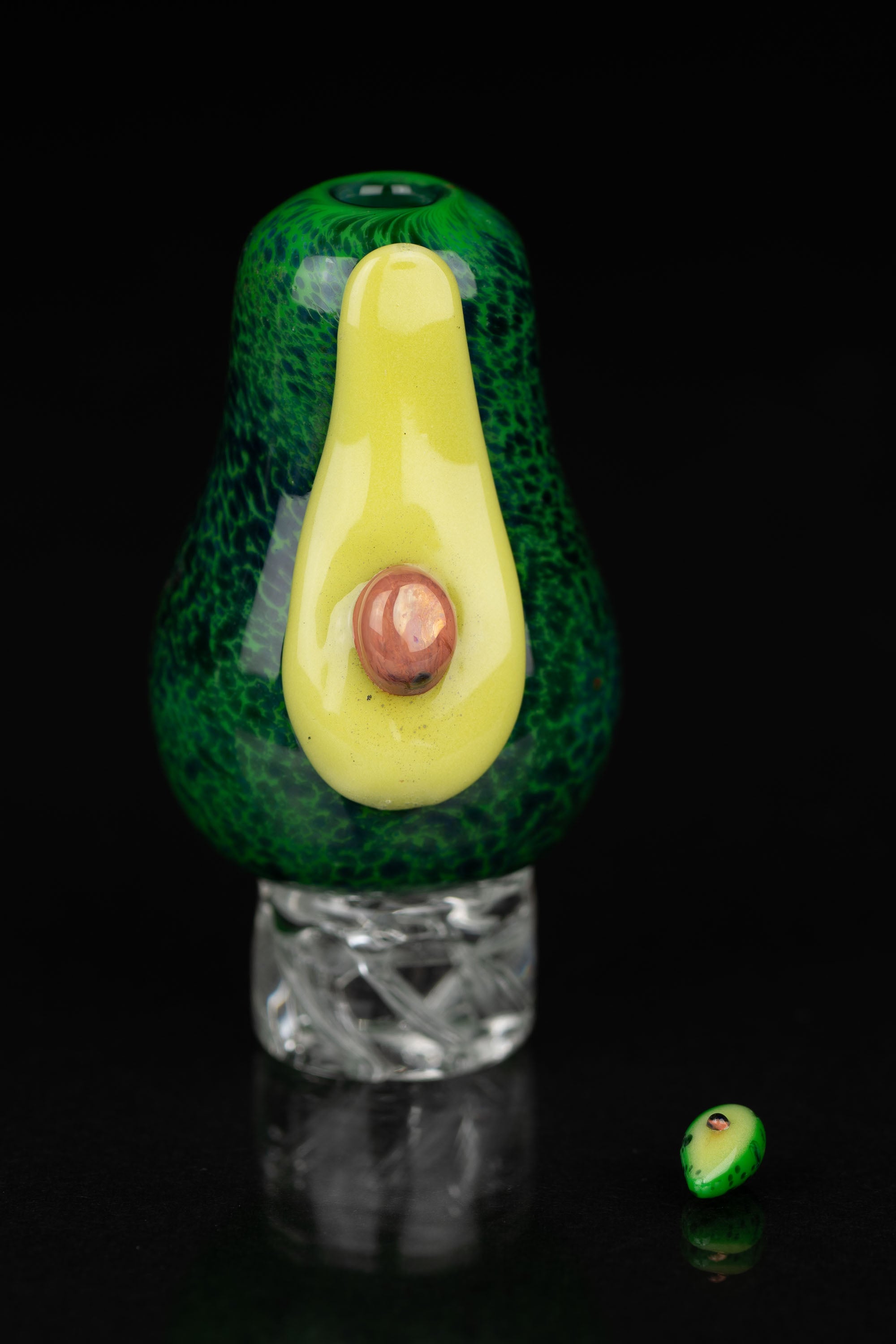 Green and yellow glass avocado-shaped dab rig with a clear base, reflecting on a black surface.