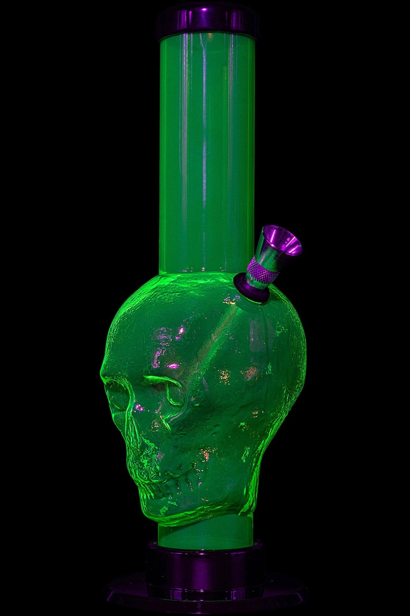 Green glass skull-shaped water pipe with a purple mouthpiece, illuminated in the dark.