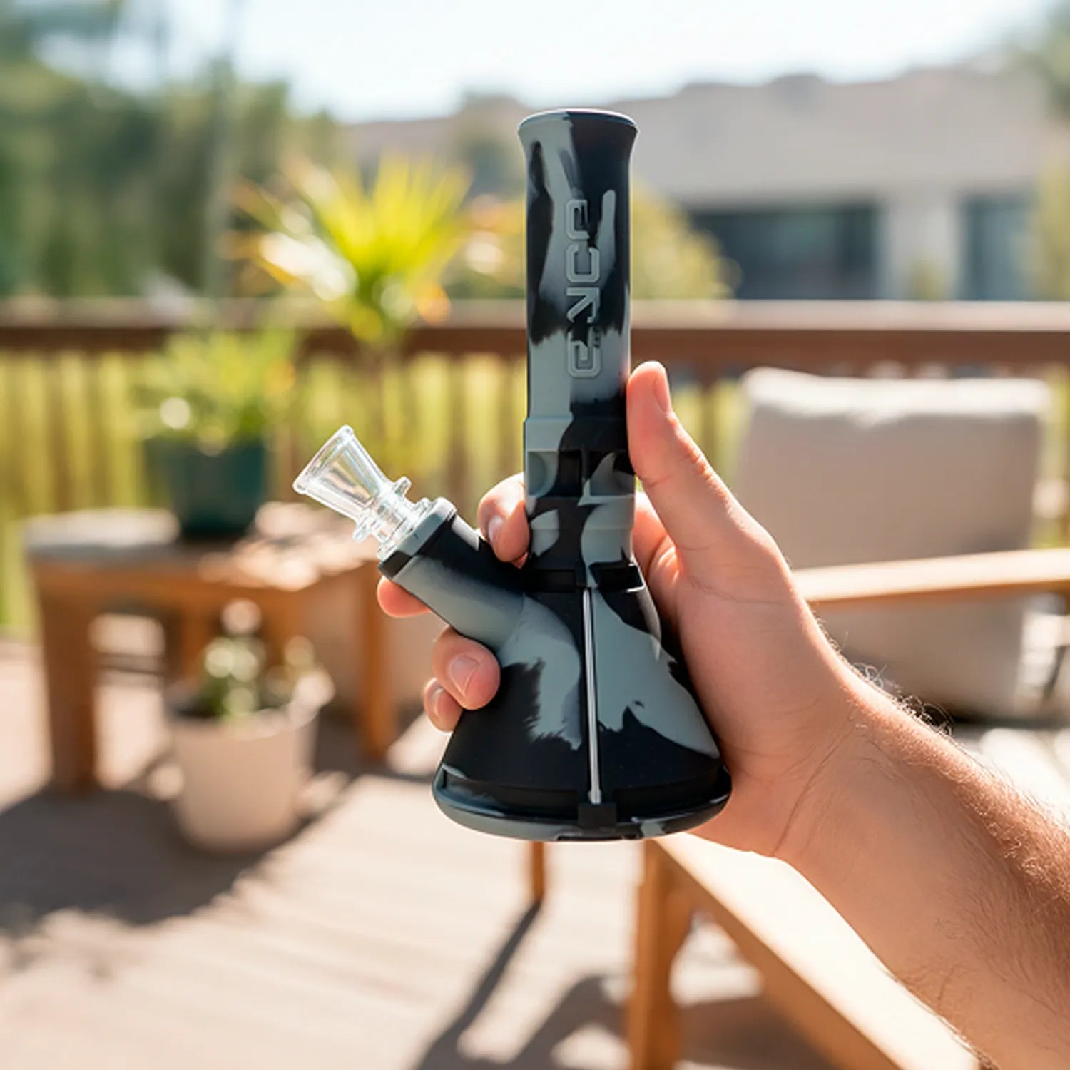 Handheld outdoor shot of a black-and-gray patterned Eyce Mini Beaker held upright with sunlight and blurred patio background