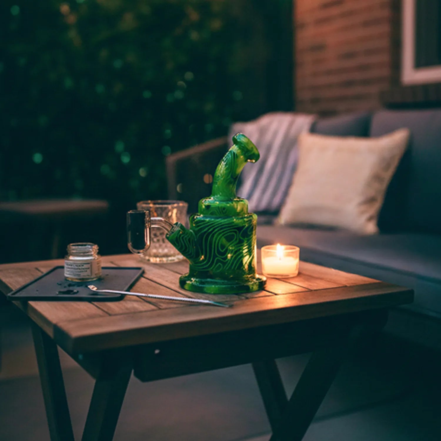 Close-up of a green marbled Eyce ORAFLEX Rig on a wooden table beside a lit candle and glassware.