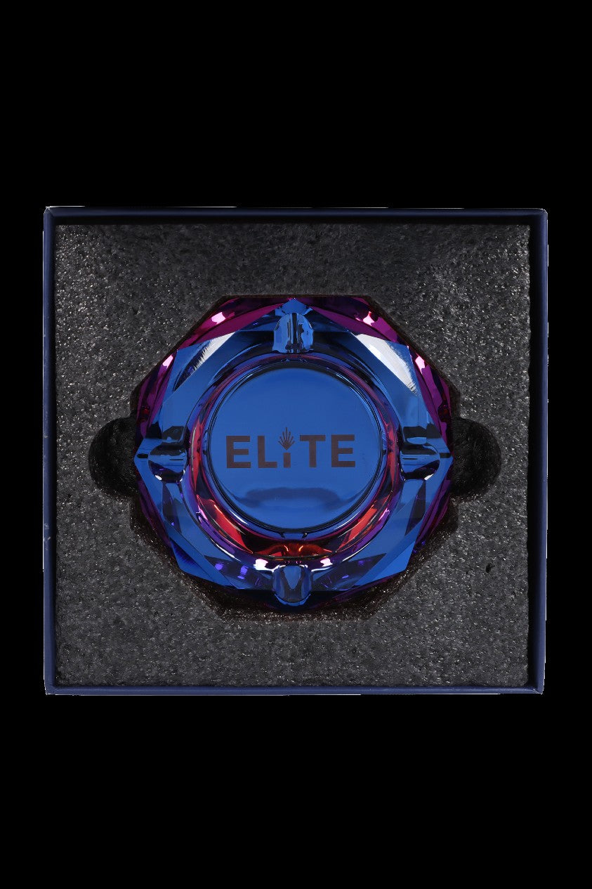 A vibrant blue and purple glass cannabis water pipe labeled “Elite” rests inside a black foam-lined box.
