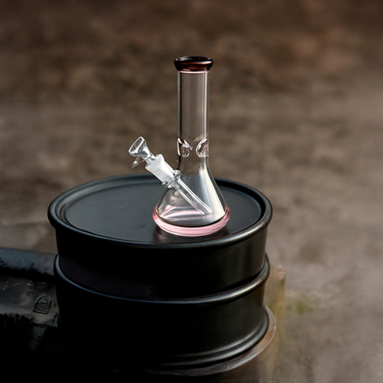 Front three-quarter view of the Smoke Cartel 9mm Big Base Beaker w/ Color Accents Bong - 12 in. showing clear glass with pink accents on a black drum.