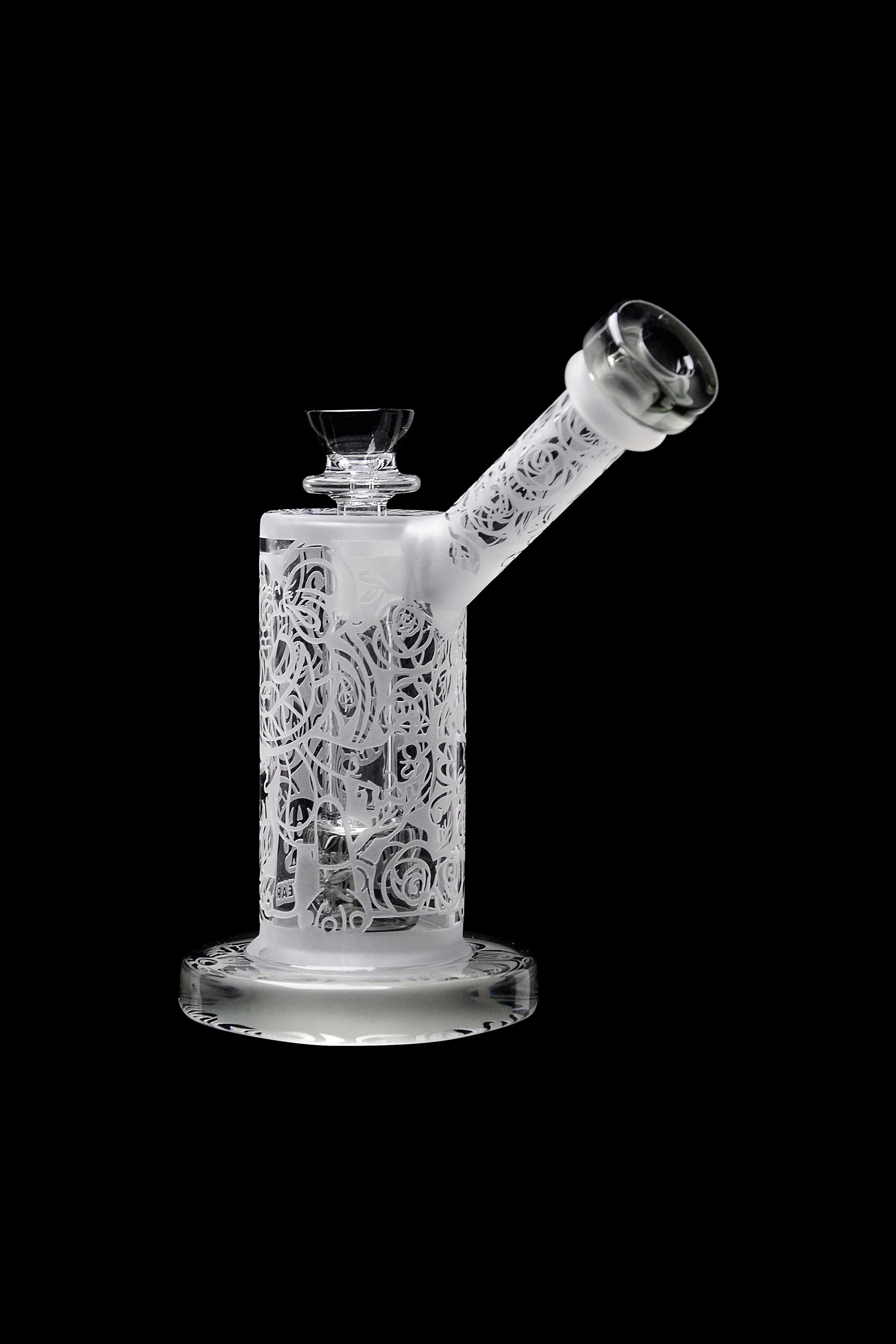 Frosted glass water pipe with intricate floral carvings, isolated on a black background.