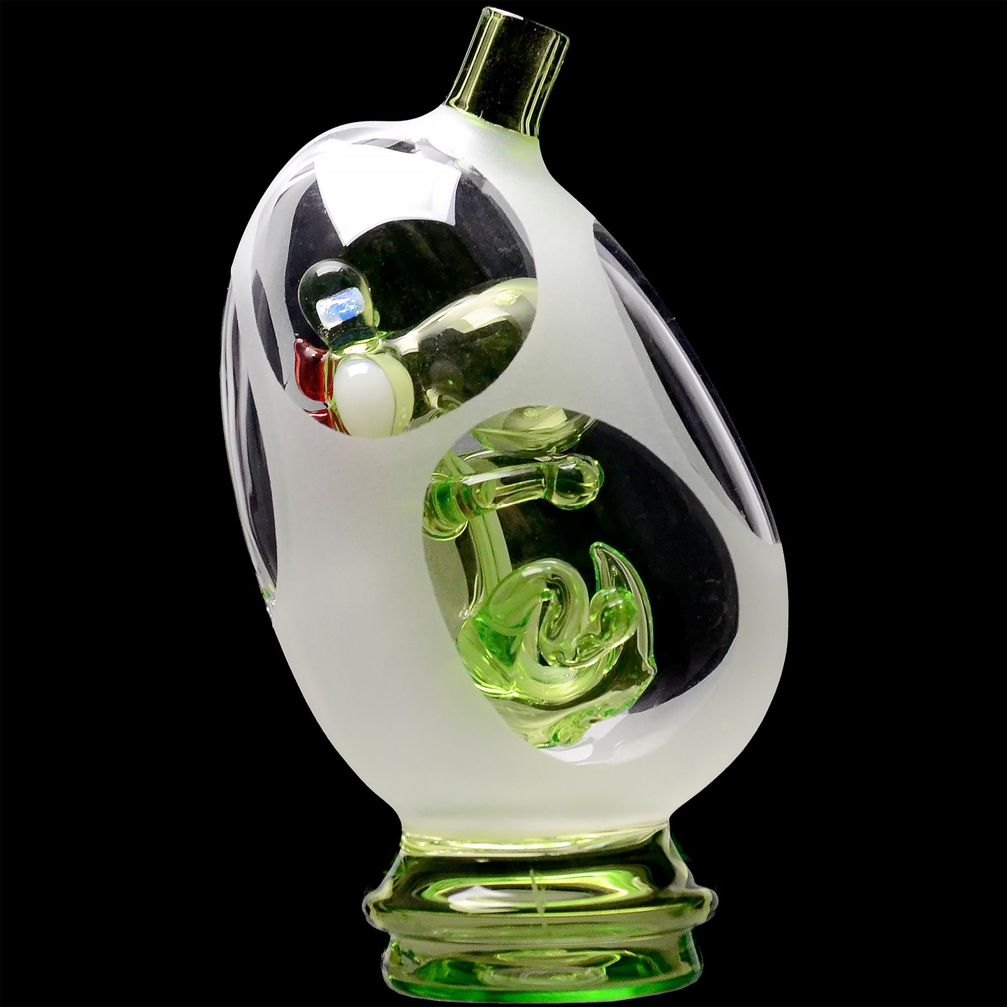 Close-up angled view of the Glassic Frosted Dino Egg Puffco Peak Glass Attachment showing frosted outer glass and a green sculpted dino encased against a black background