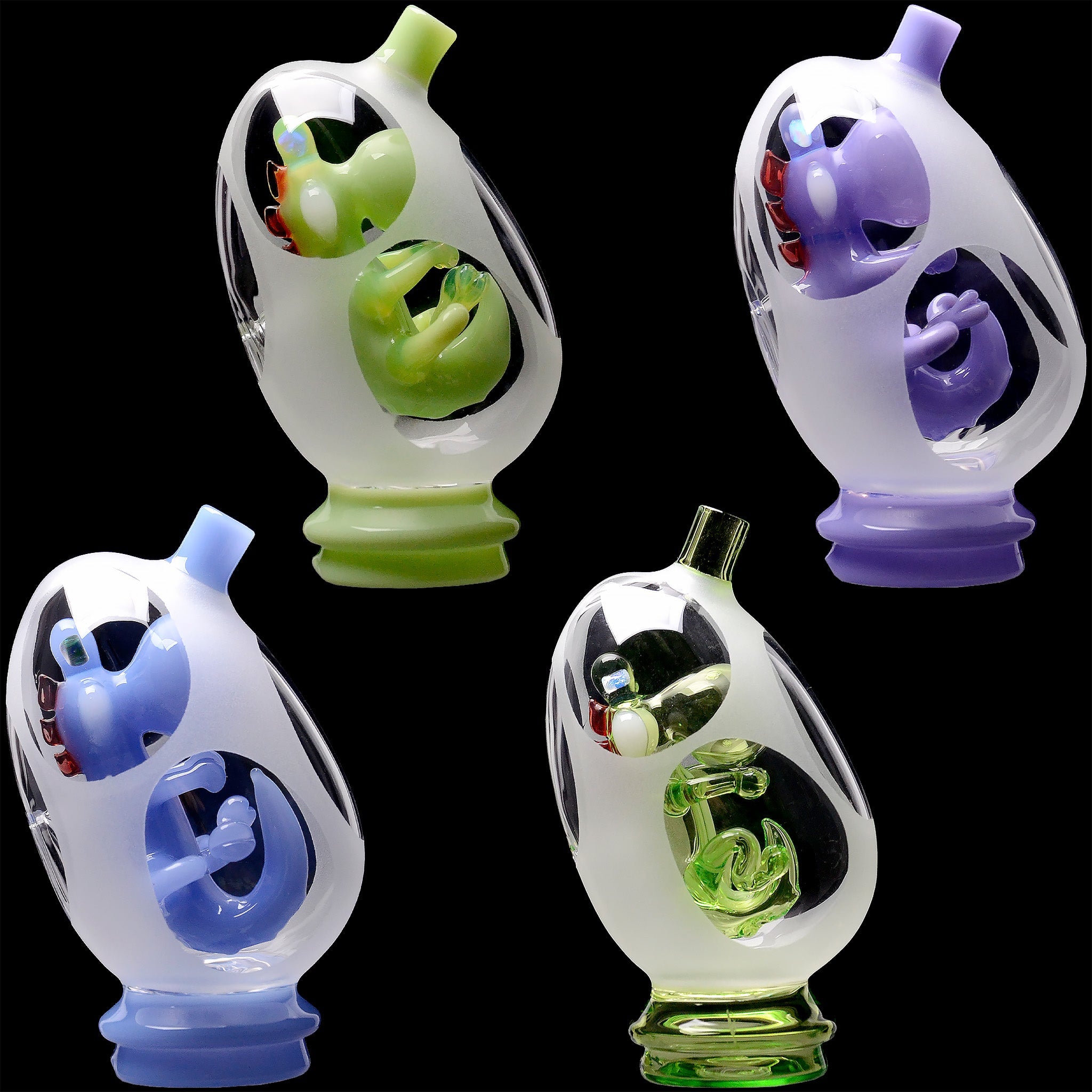 Close-up on two frosted egg-shaped Glassic Frosted Dino Egg Puffco Peak Glass Attachment pieces with green and purple inner dinosaur figures against a black background