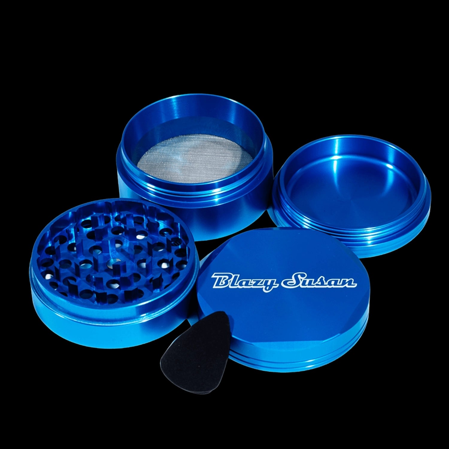Angled close-up of a disassembled blue Blazy Susan 4-pc 3 Chamber Grinder showing the anodized lid with logo, toothed grinding plate, mesh chamber, and catch tray.