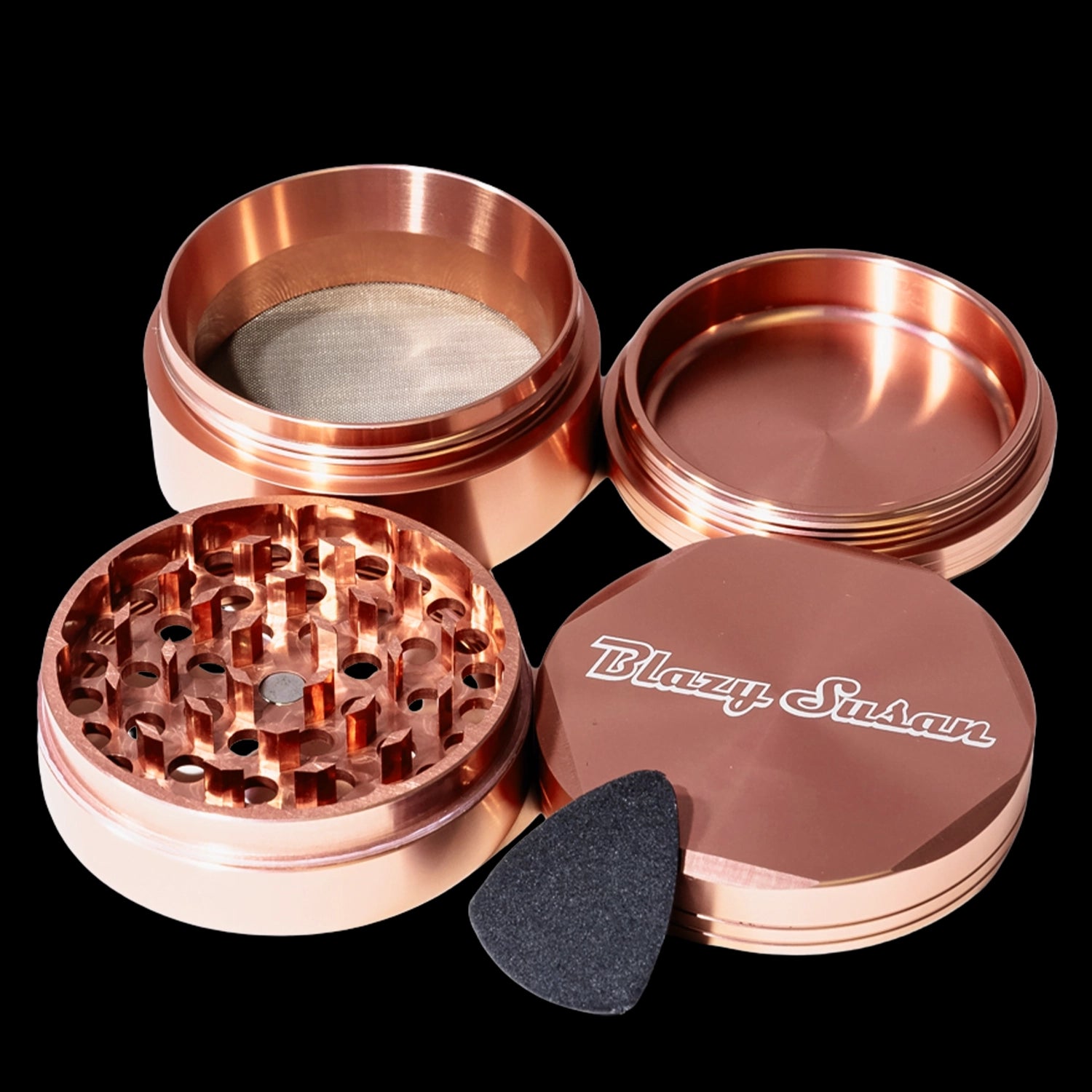 Close-up top-down view of the rose gold Blazy Susan 4-pc 3 Chamber Grinder showing its four separated pieces, grinding teeth, mesh screen, and branded lid.