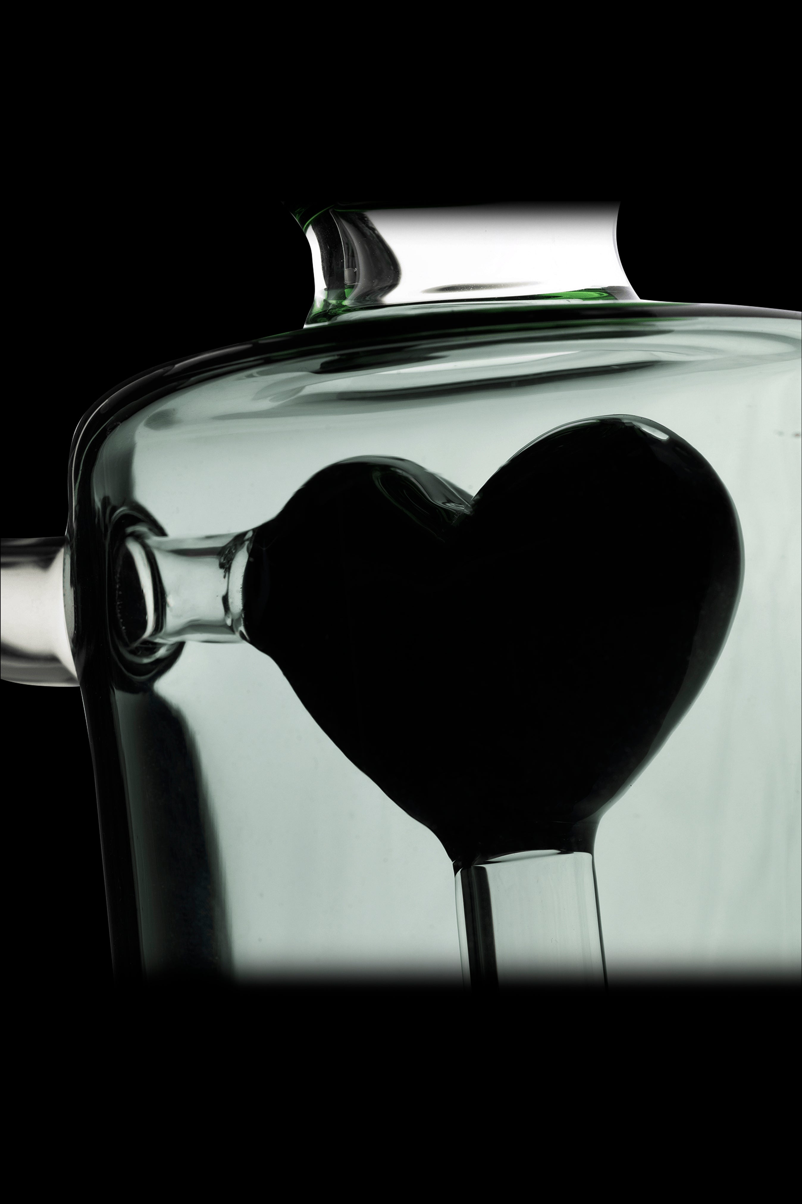 A glass cannabis water pipe shaped like a heart, silhouetted against a pale green background.