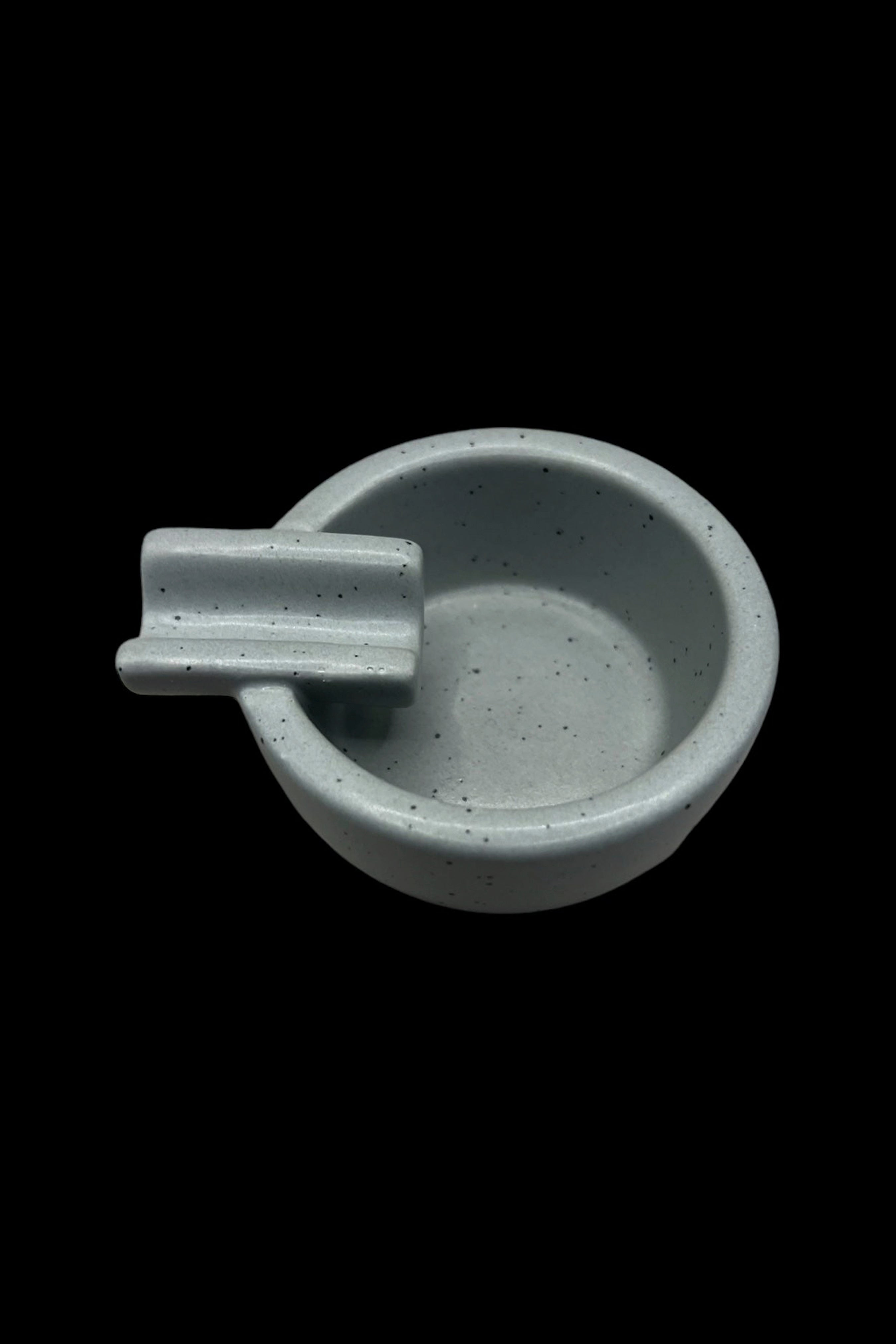 Ceramic cannabis ashtray with a built-in rest for joints or cigarettes, in a muted teal color.