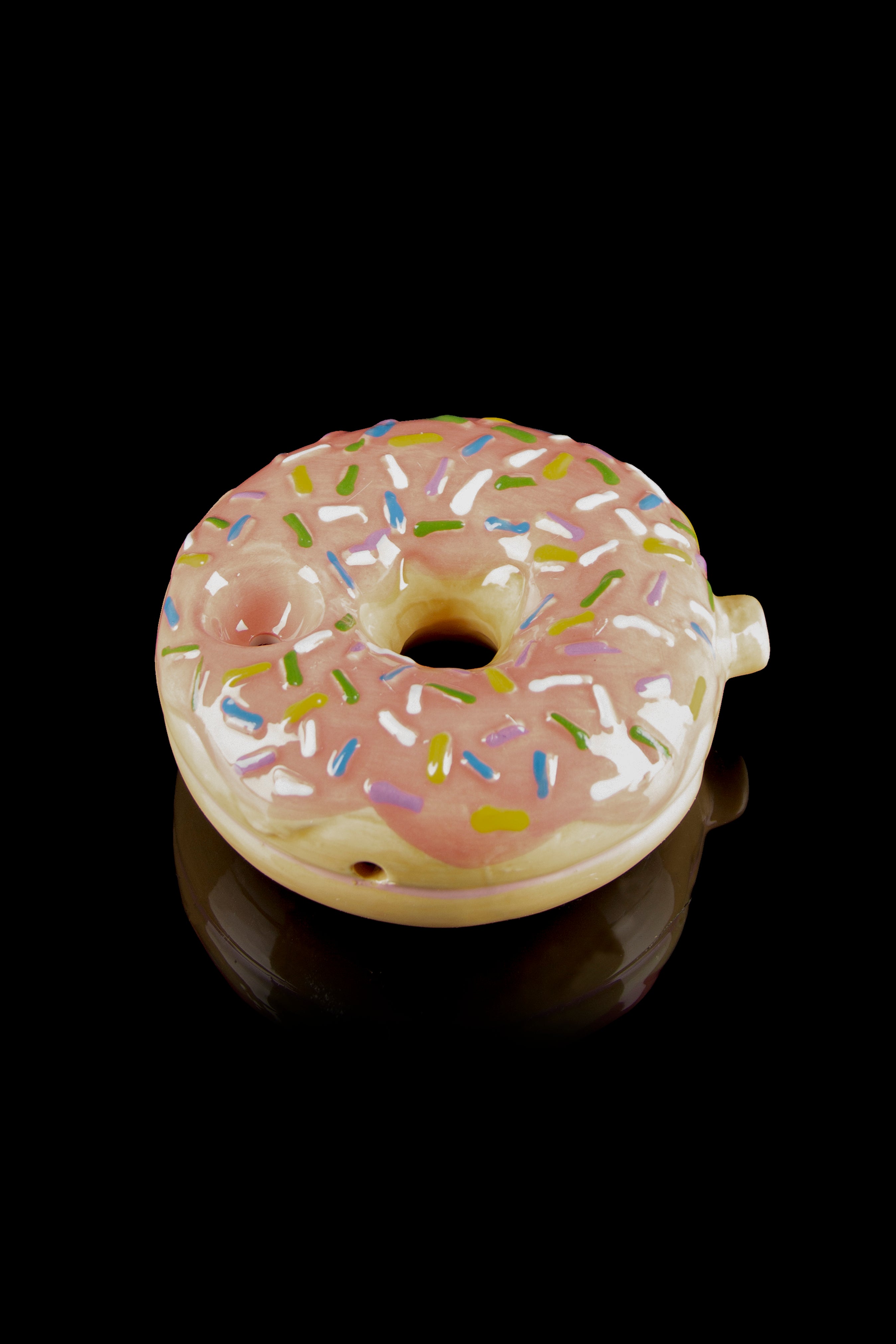 Pink glazed donut-shaped glass piece with colorful sprinkles, reflecting on a dark surface."