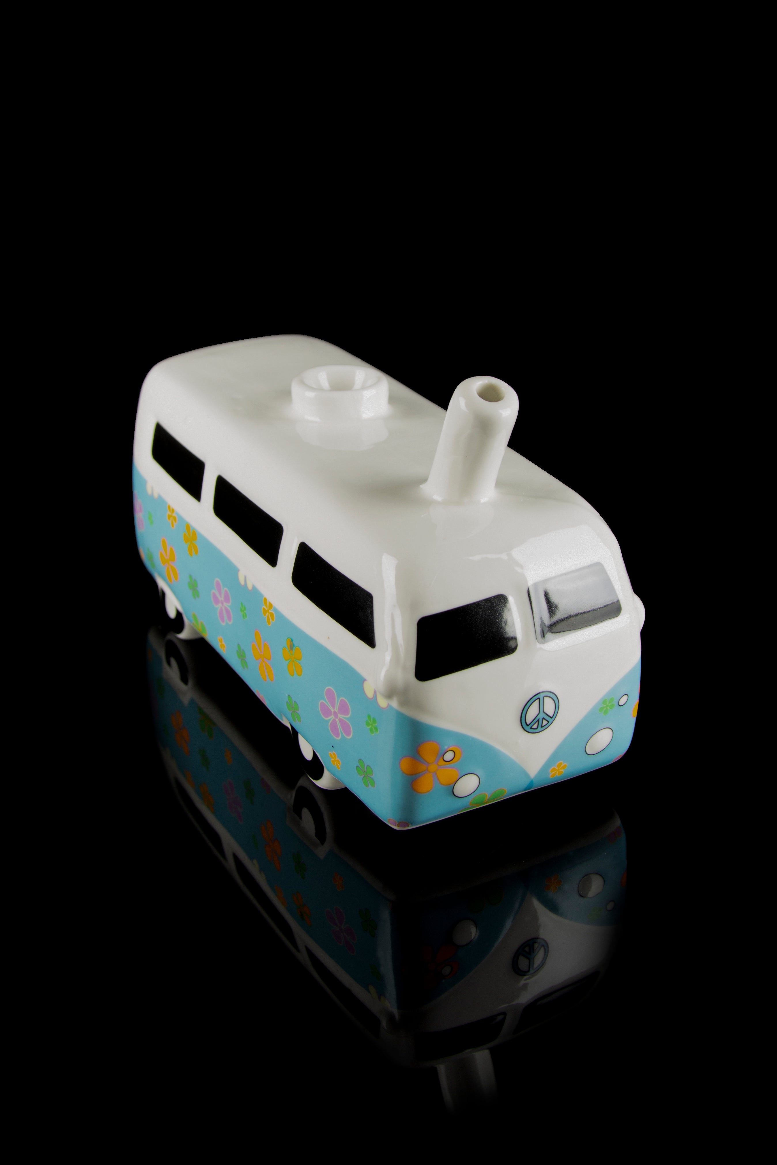 Ceramic VW-style bus water pipe with floral and peace sign details, reflecting on a black surface.