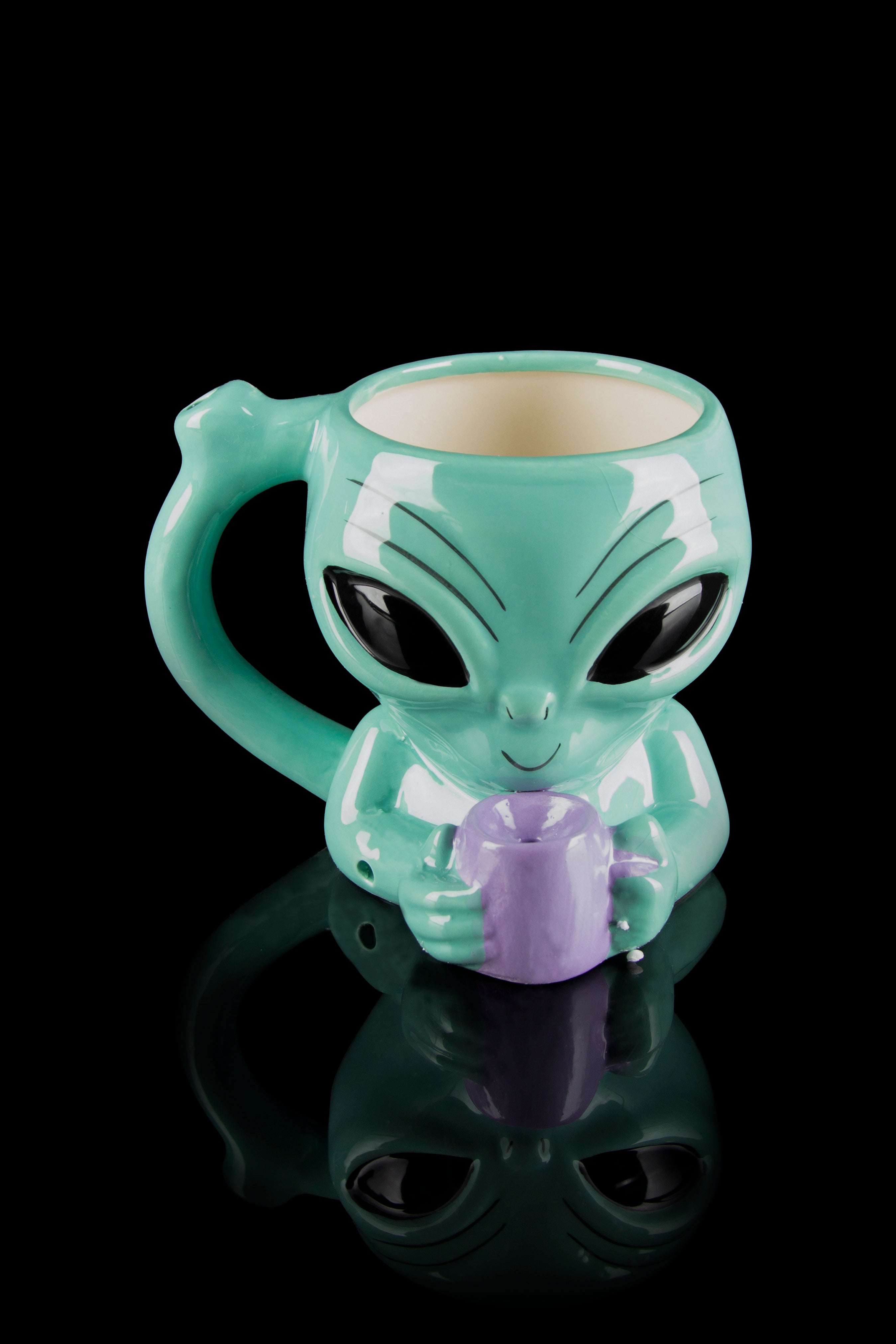Green alien-shaped ceramic mug holding a purple cannabis bud, reflected on a black surface.