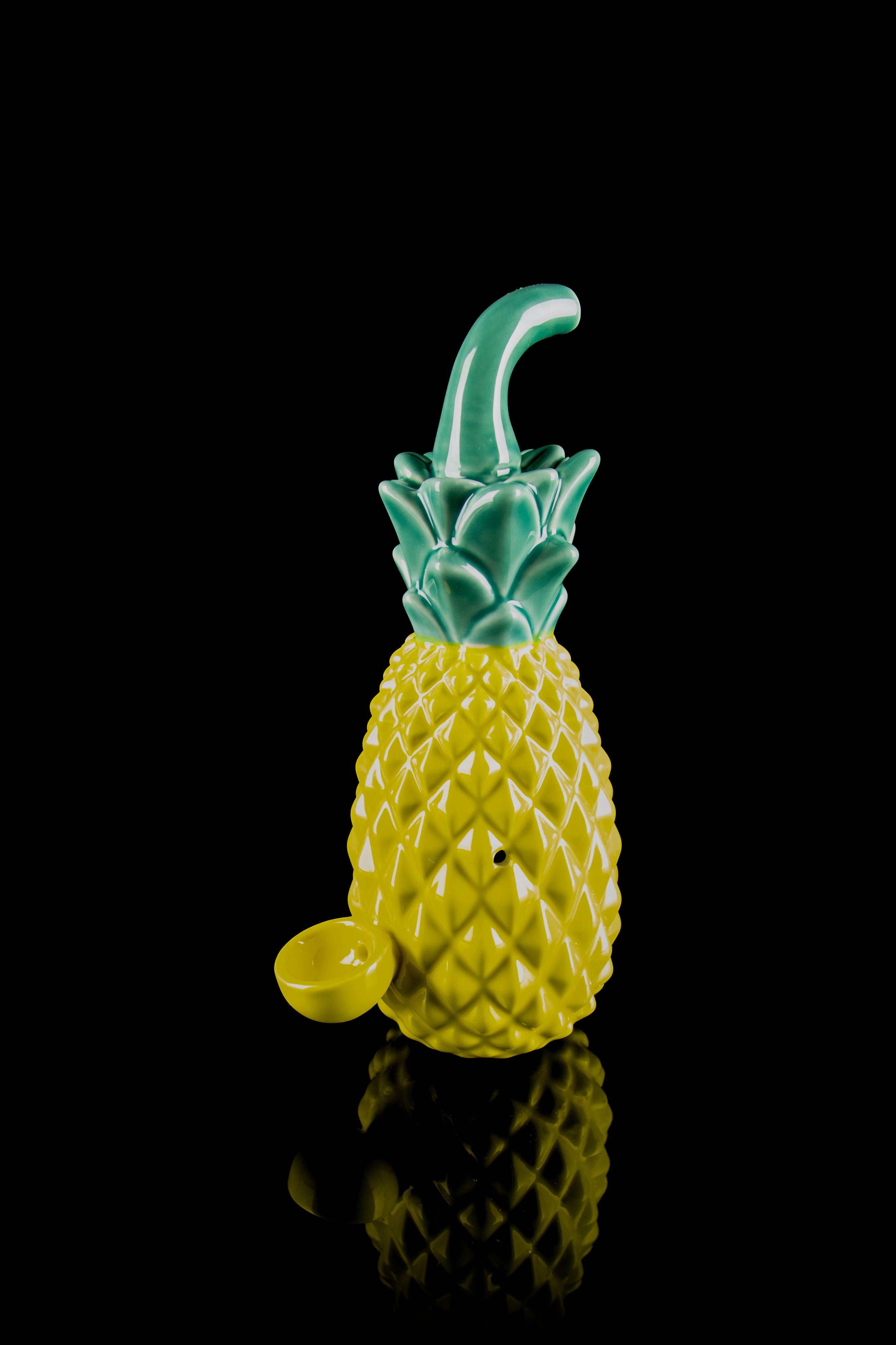 Yellow glass pineapple water pipe with green accents, reflecting on a black surface.