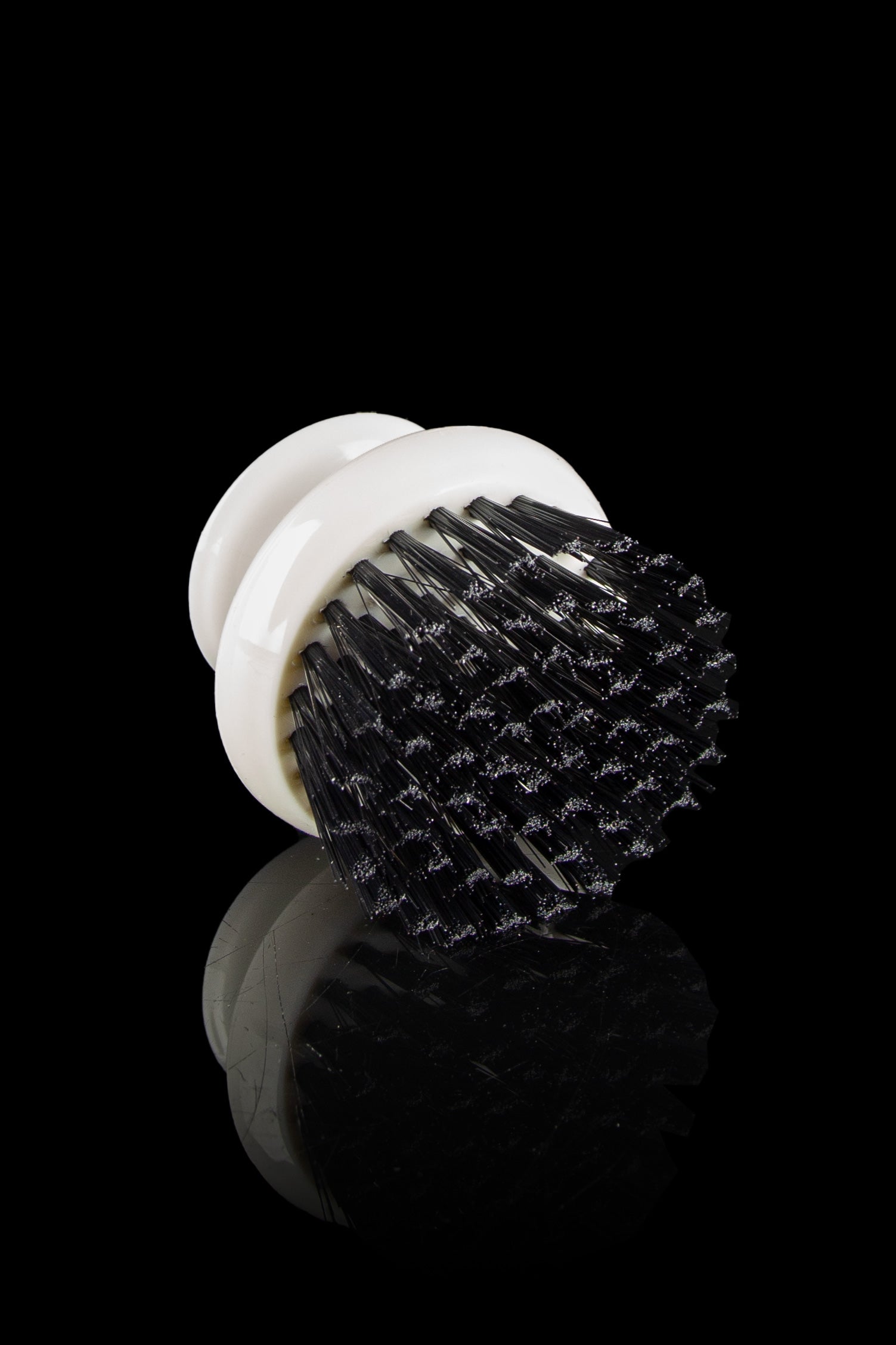 White pipe cleaning brush with black bristles, displayed on a reflective surface against a black background.