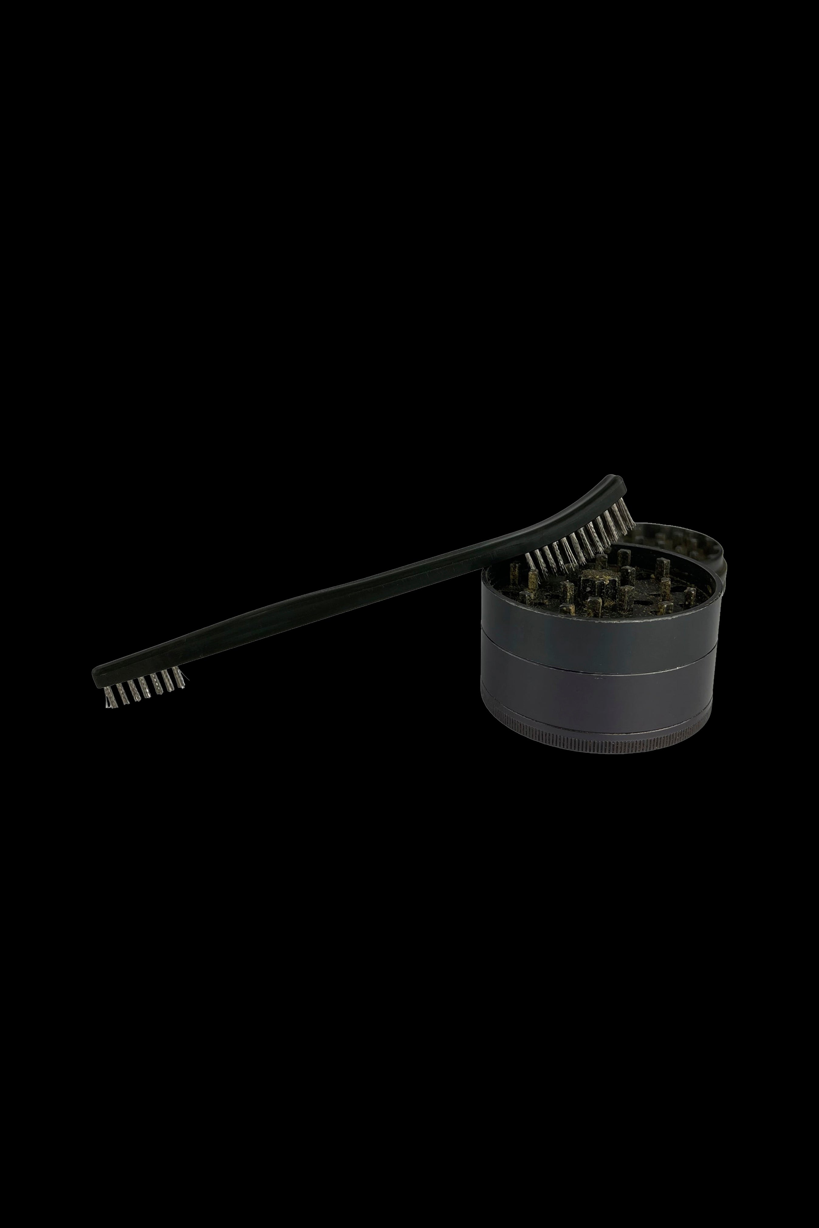 Black cannabis grinder with cleaning brush on a dark background.