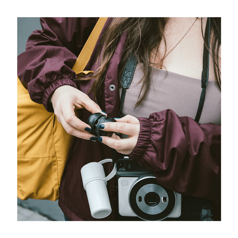 Person adjusting a white cannabis vape pen attached to a camera strap.