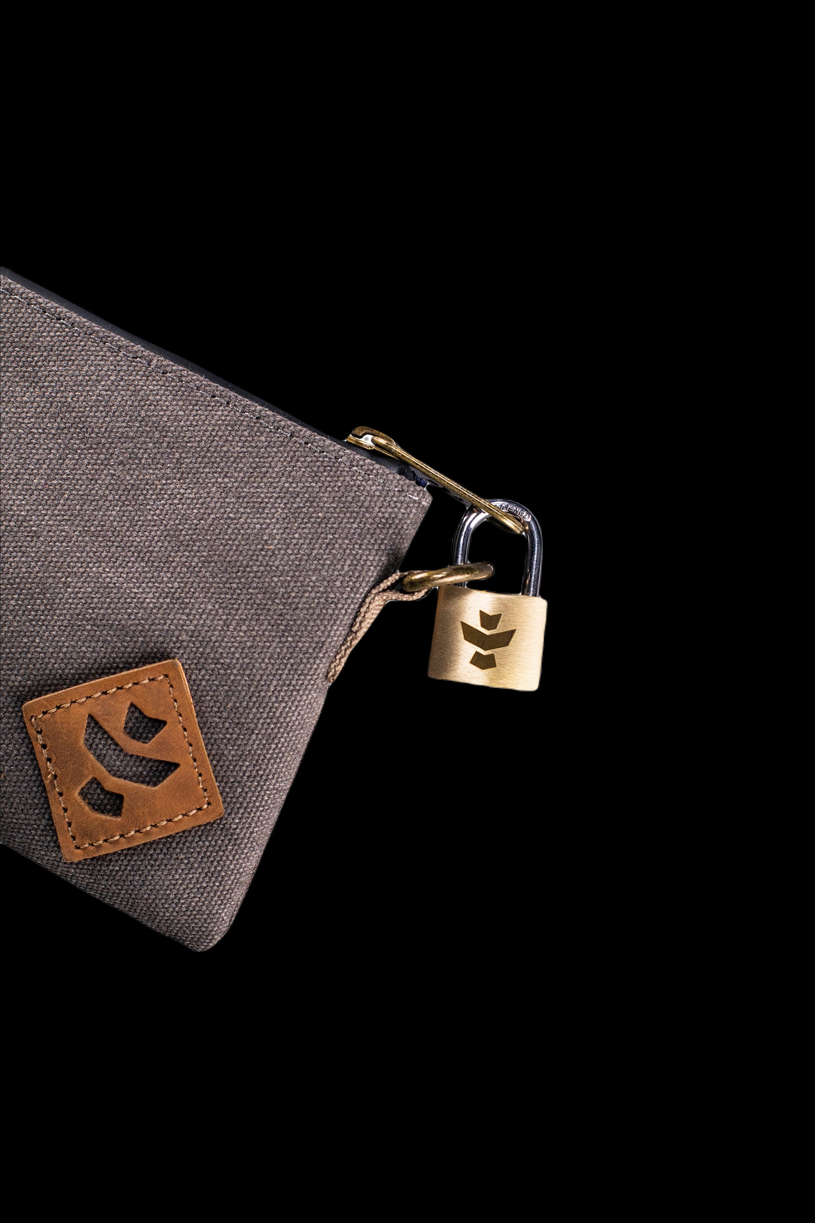 Close-up angled view of the sage Revelry Supply Smell Proof Zippered Small Stash Bag - The Mini Broker showing its textured fabric, leather patch, zipper pull, and small brass padlock against a black background
