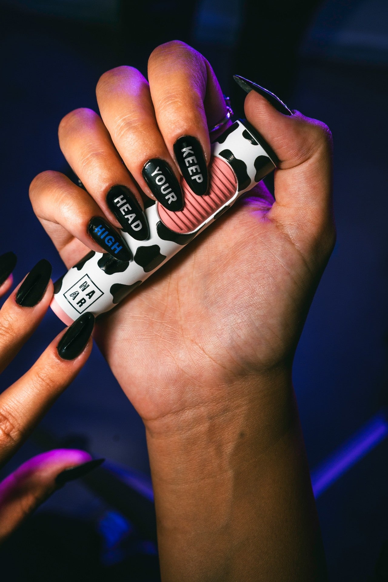 Close-up of a hand with black and white cow-print nails spelling out "Keep Your Head High" and "MAR" in black text.