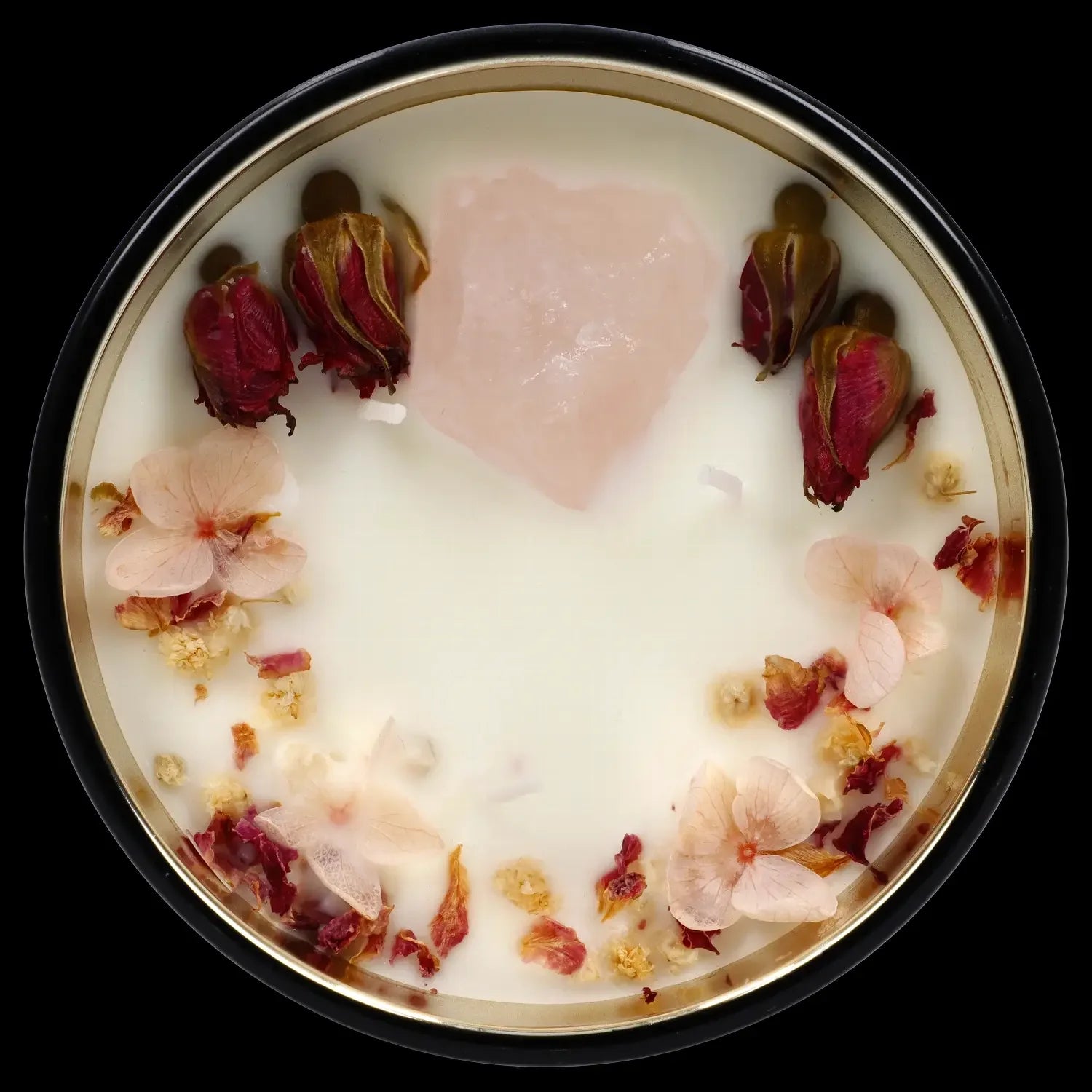 Overhead view of a white cannabis concentrate with scattered red and pink flower petals in a circular container.