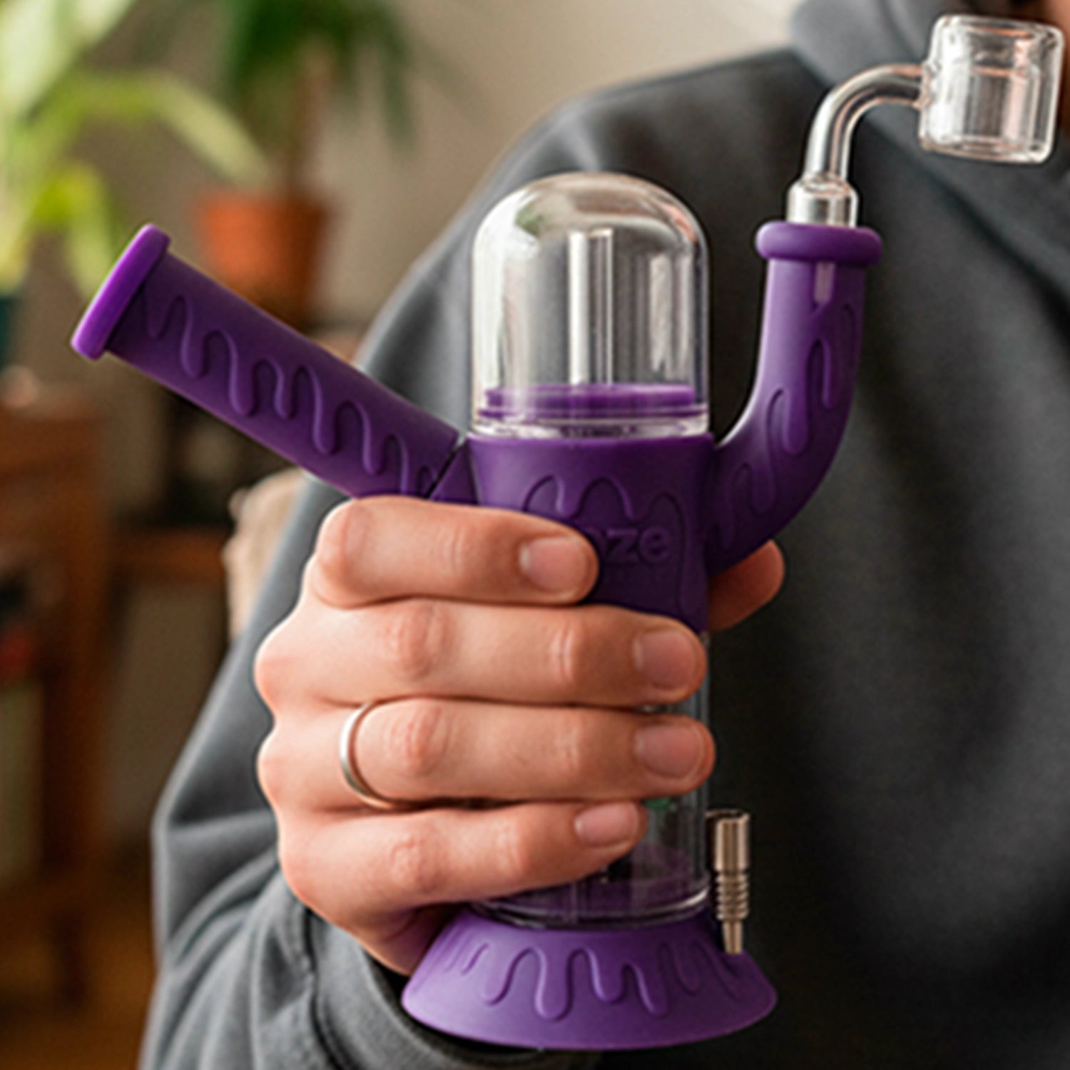 Handheld close-up of an Ooze "Cranium" Silicone 4-in-1 Glass Bong in scarlet-purple, showing its dome, angled arm, and textured grip.