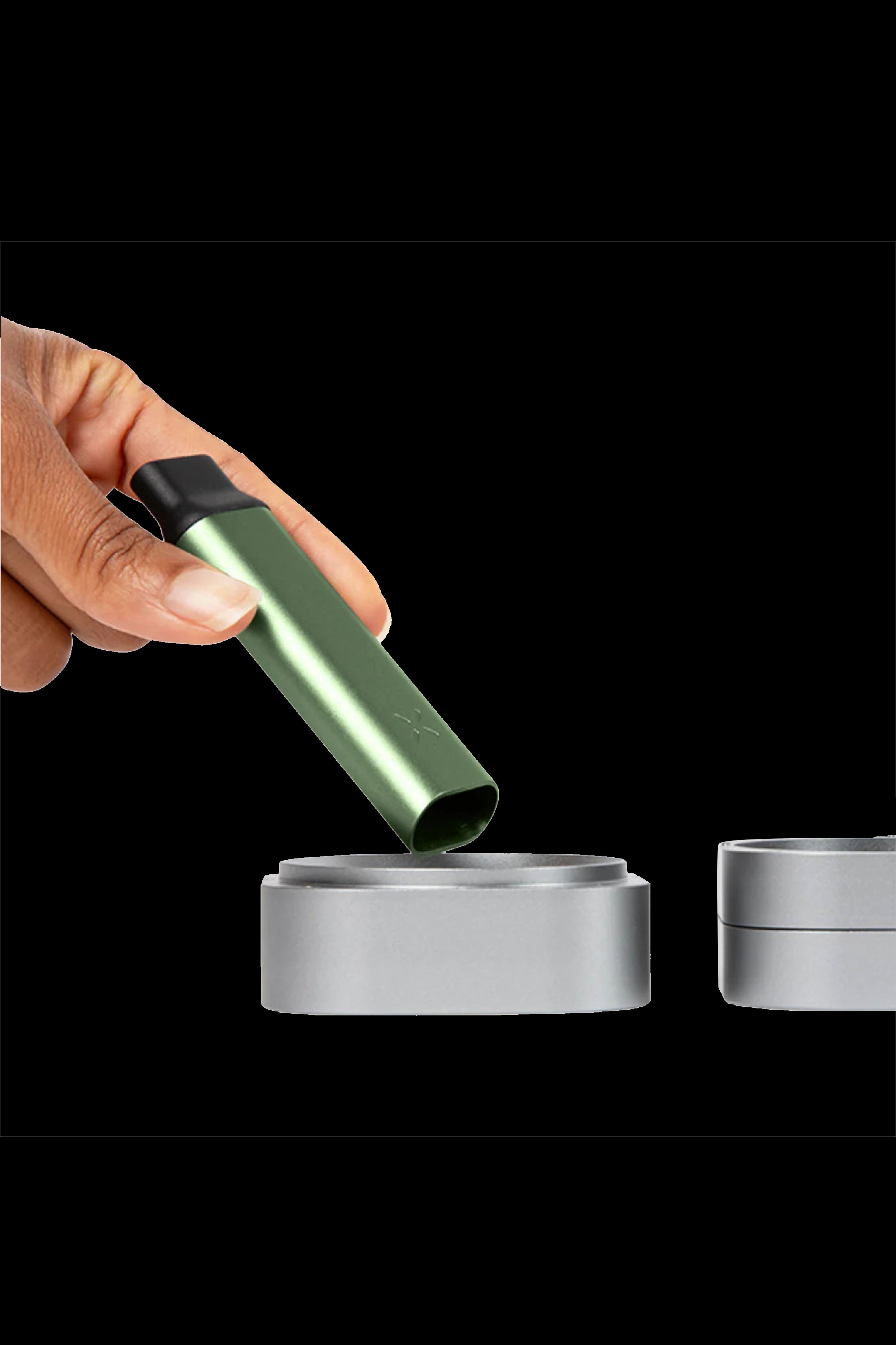 Green cannabis vape pen being inserted into a silver charging base, with a second base visible beside it.