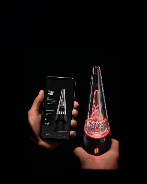 Hands holding a Puffco New Peak Pro with 3D XL Chamber beside a smartphone showing its companion app, both lit by red accent lighting on a black background.