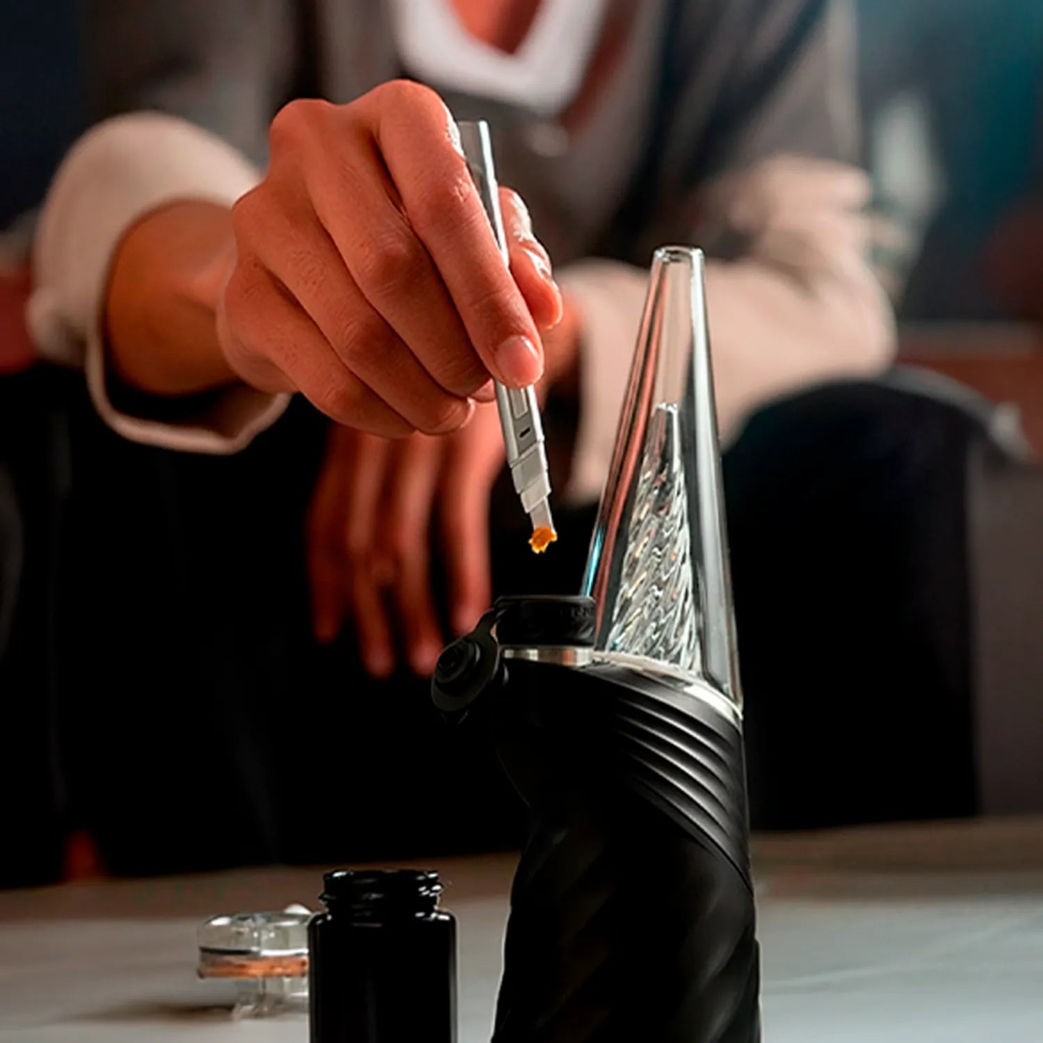 Close-up angled shot of a hand loading the Puffco New Peak Pro with 3D XL Chamber, the black device's textured body and clear conical chamber in soft indoor light