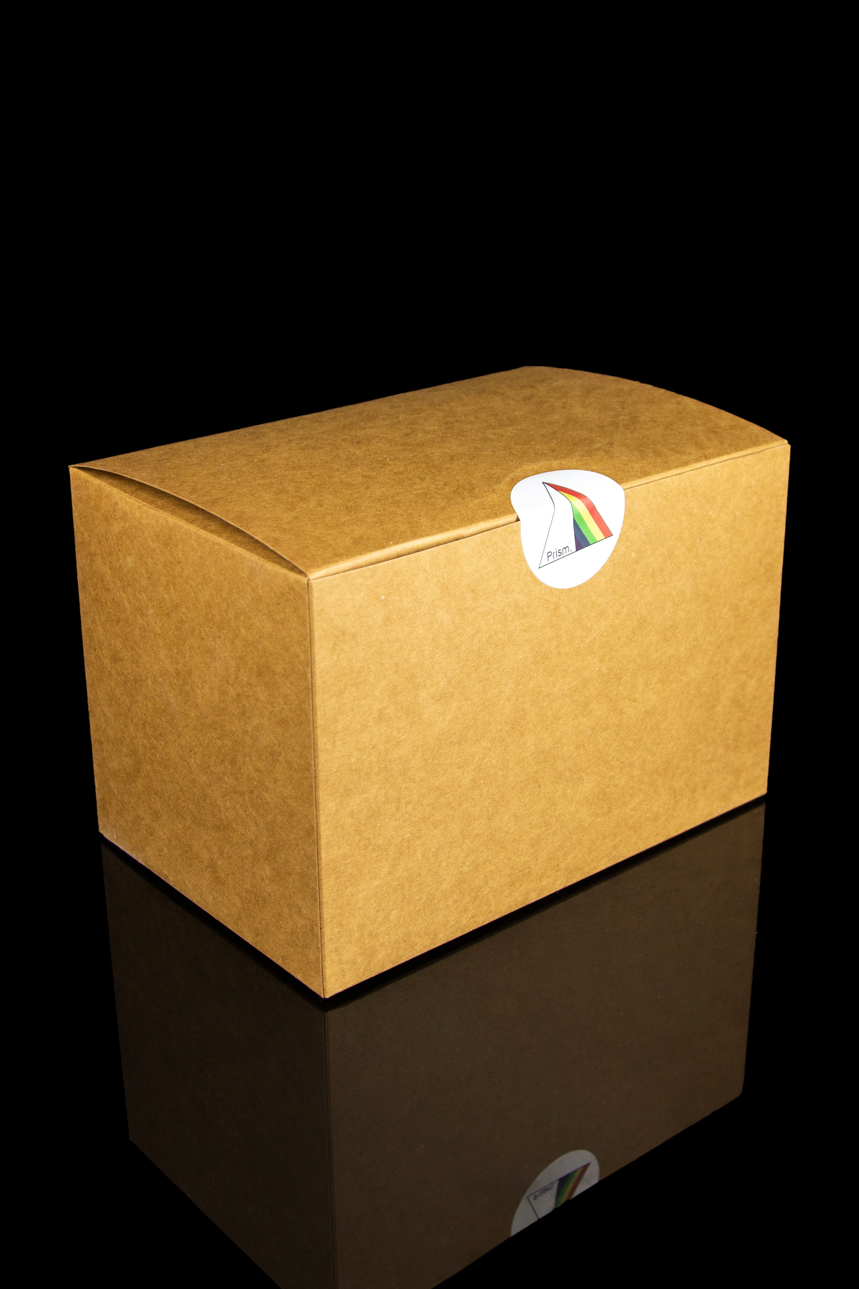 Brown shipping box with a colorful "Prism" sticker, reflecting on a glossy surface.
